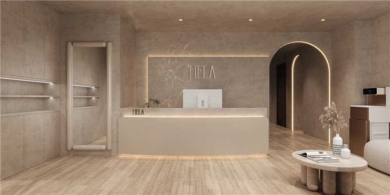 Modern reception area with a beige color scheme, illuminated signage reading 'HELA' behind the counter, and minimalist decor including a round coffee table with books and vases, a textured wall, and a rounded archway leading to another room.