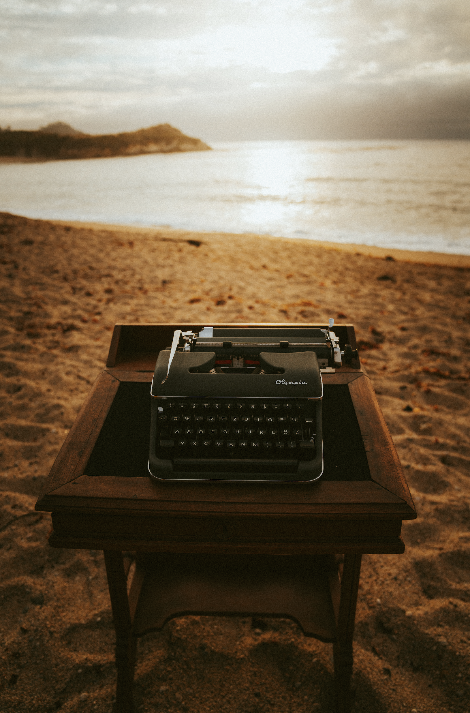 A vintage typewriter on a wooden table at the beach during sunset.