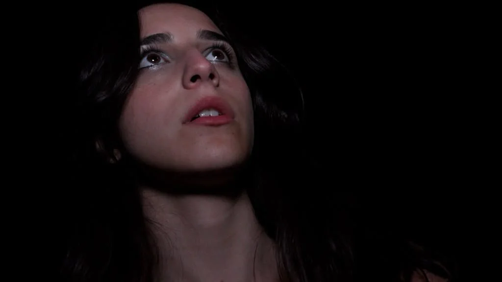 Close-up of a woman's face with dark hair looking upward against a black background.