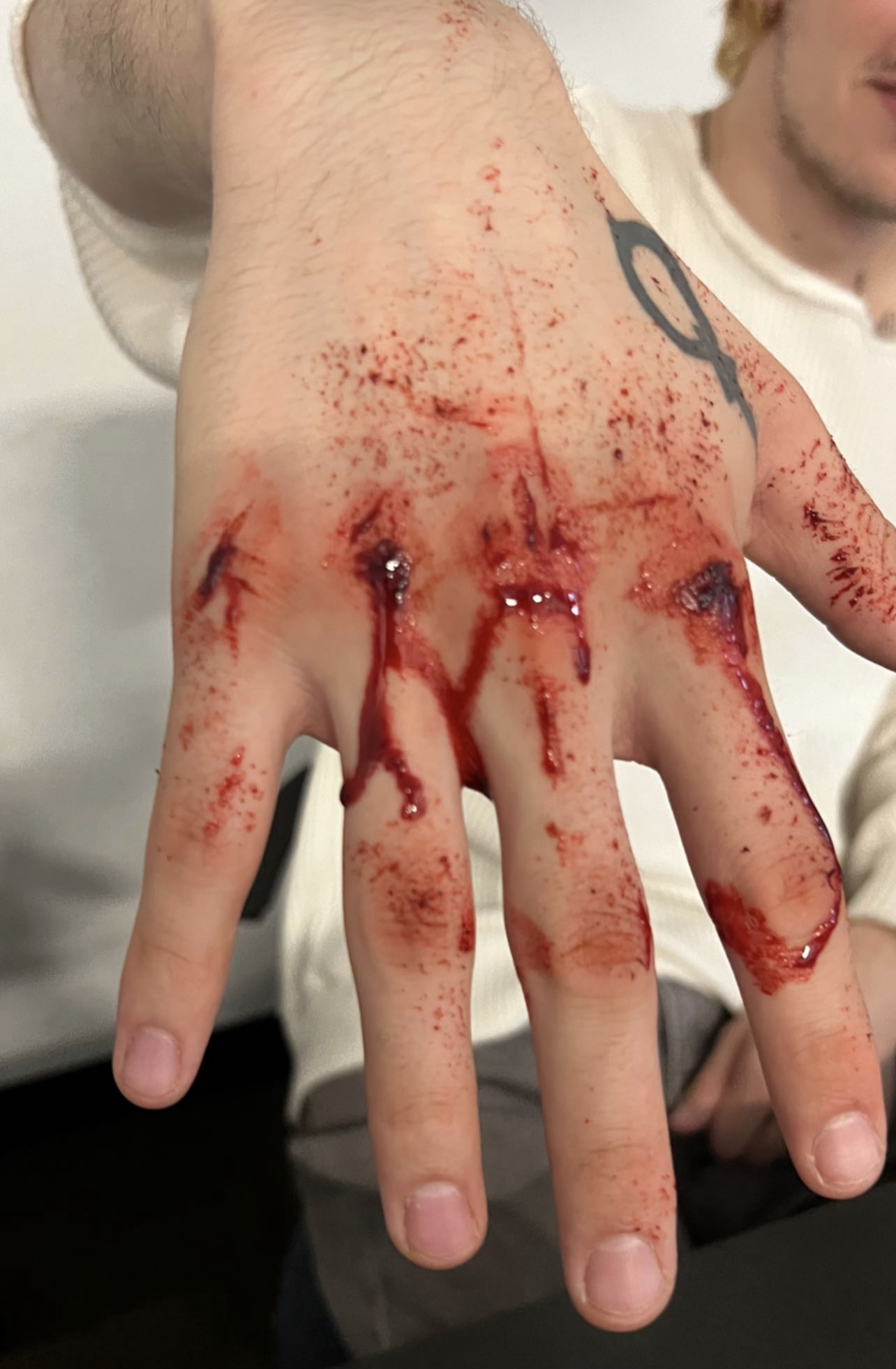 A person's hand covered in fake blood with deep cuts and wounds, likely a costume or theatrical makeup,.
