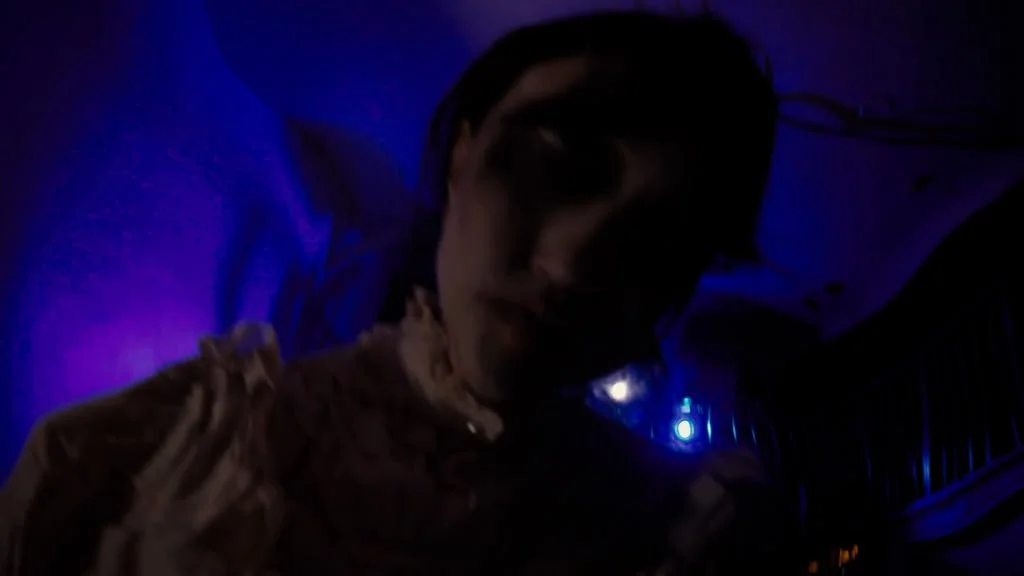 A woman with short hair in a dimly lit room with purple and blue lighting.