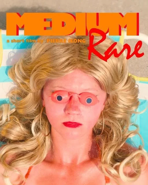 A woman with long blonde curly hair lying down wears peach-colored sunglasses and bright red lipstick, with a vintage movie poster titled 'Medium Rare' in the background.