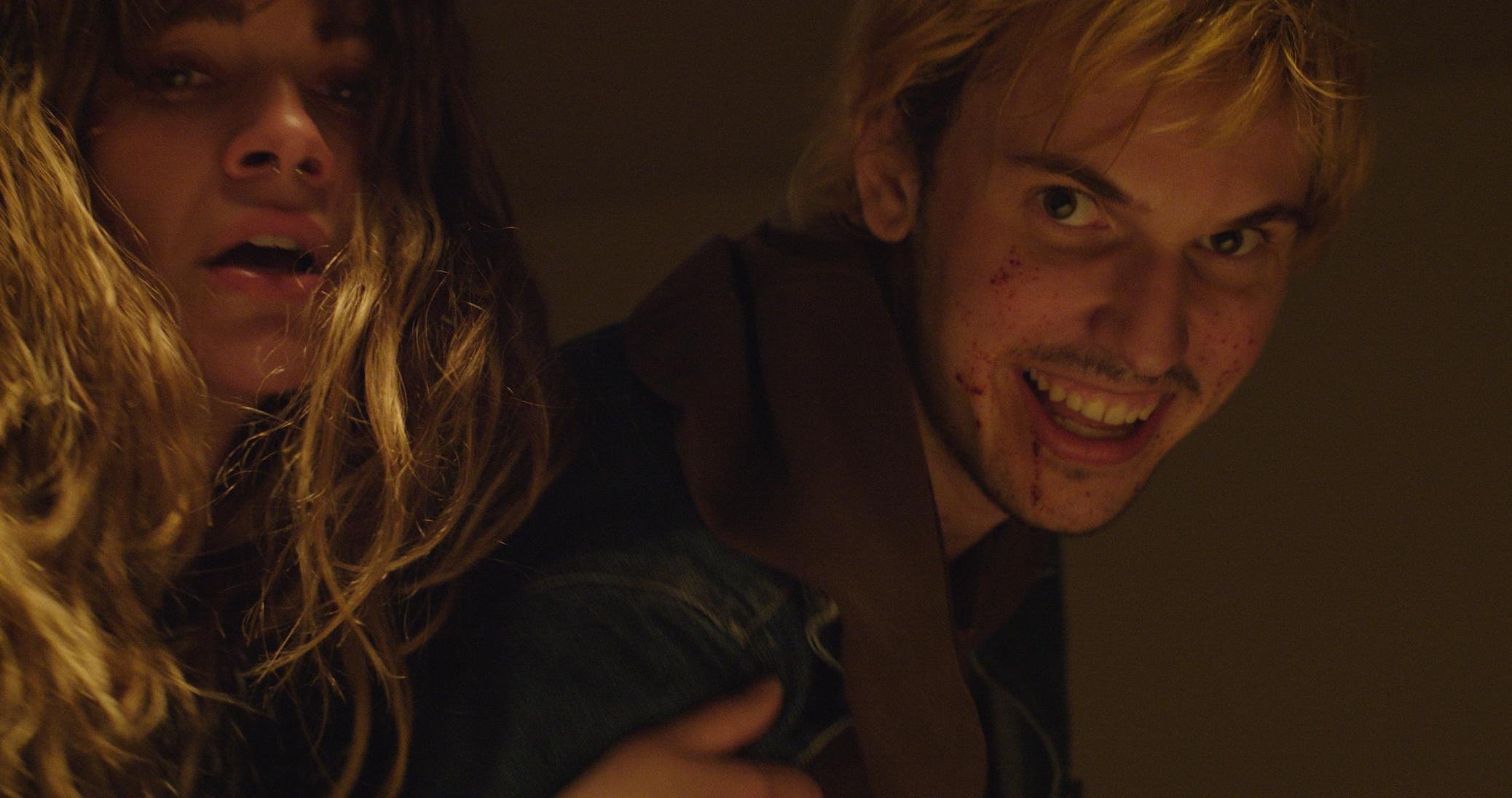 A woman with curly hair and a man with blond hair smiling in a dark setting.