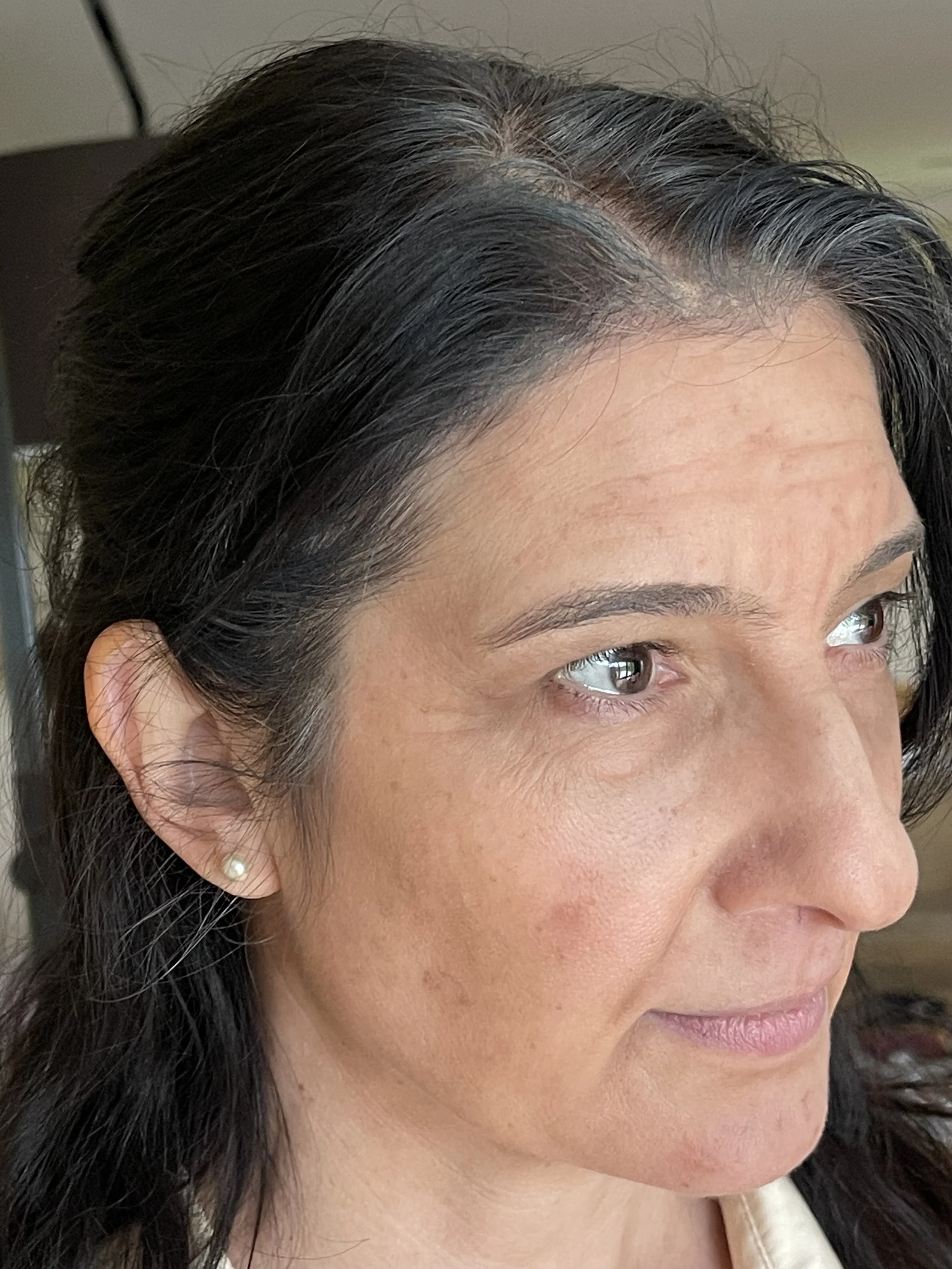Close-up of a woman's face showing her right eye, eyebrow, and ear with a pearl stud earring, and dark hair.