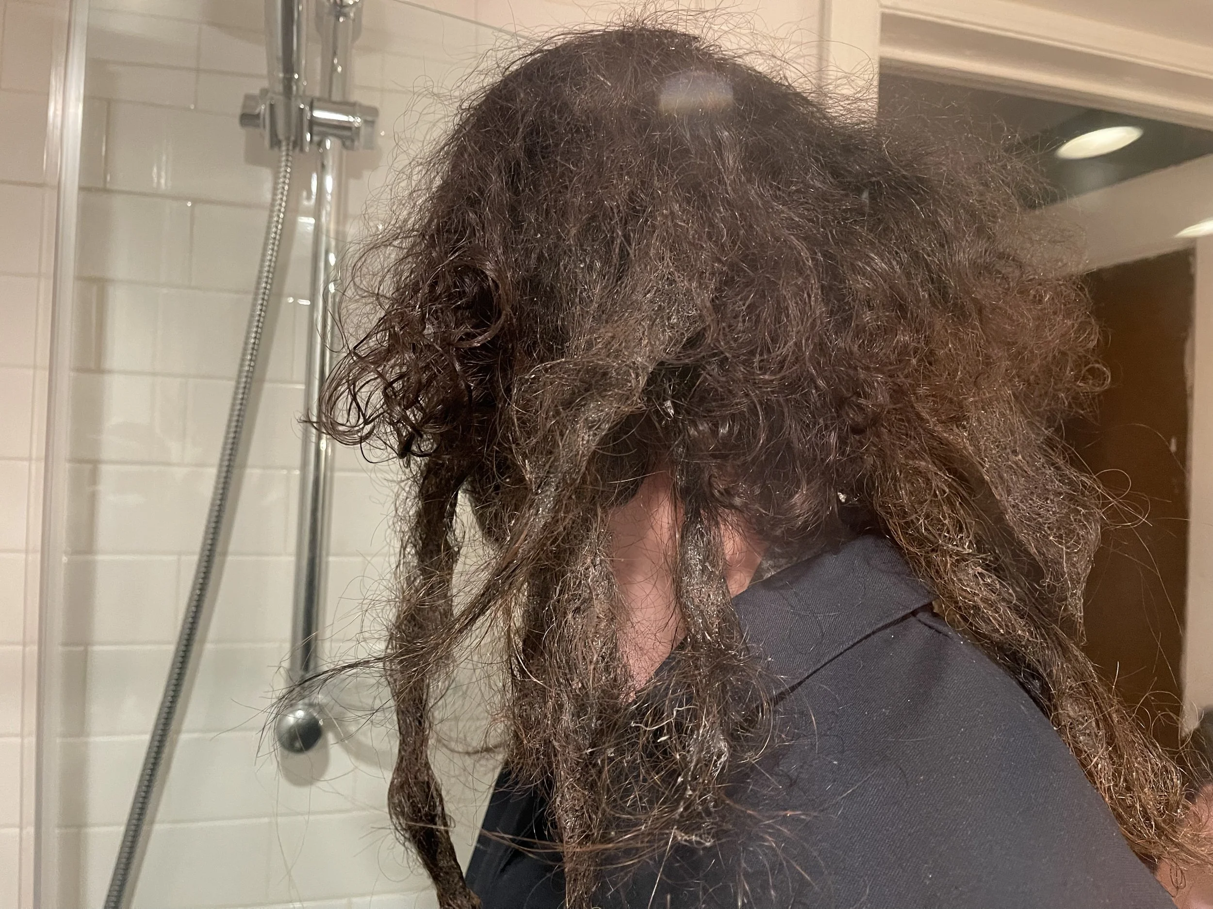Person with curly, wet hair in a bathroom, preparing to shower.