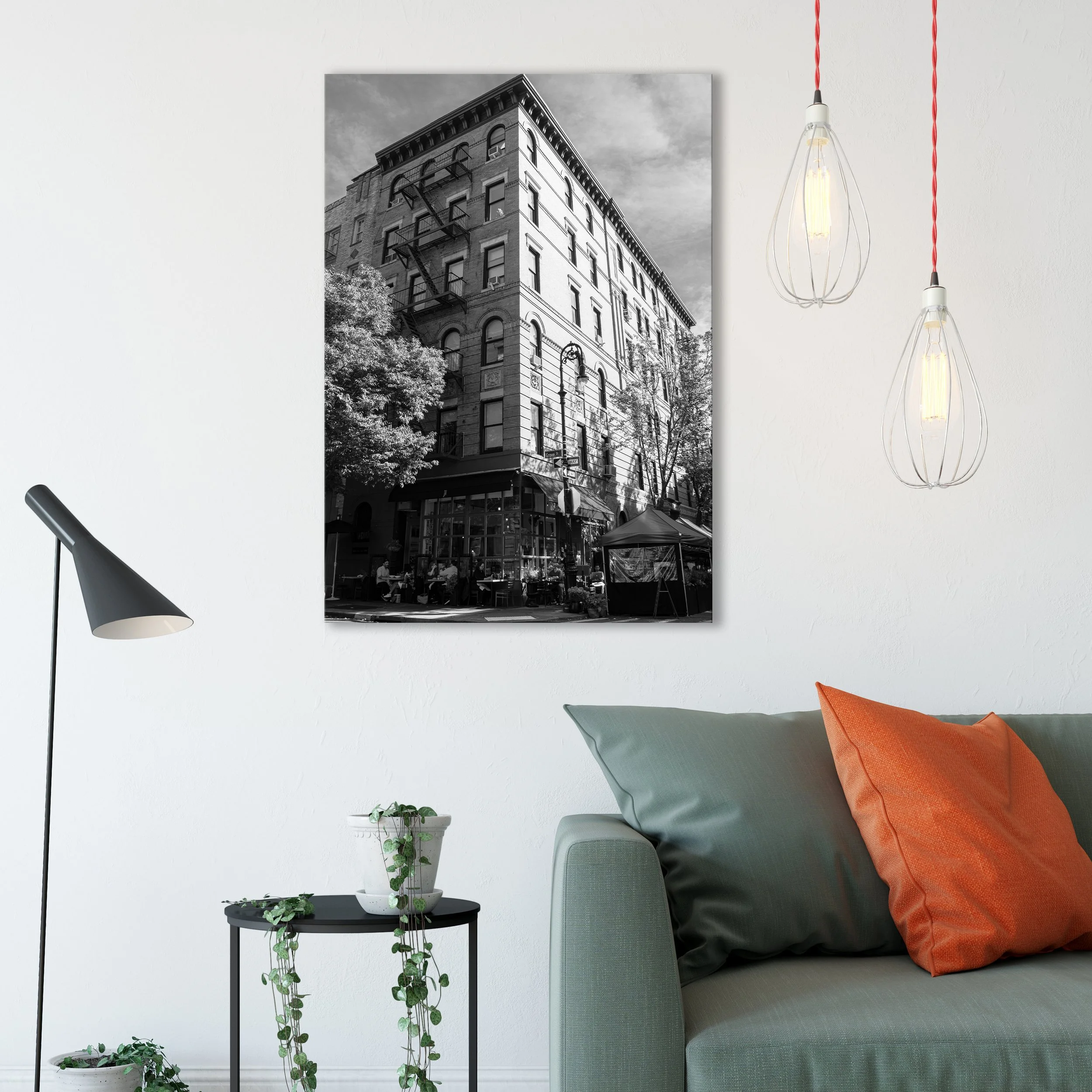 Large black and white West Village apartment photography print hanging in a modern living room above a green sofa with an orange pillow.