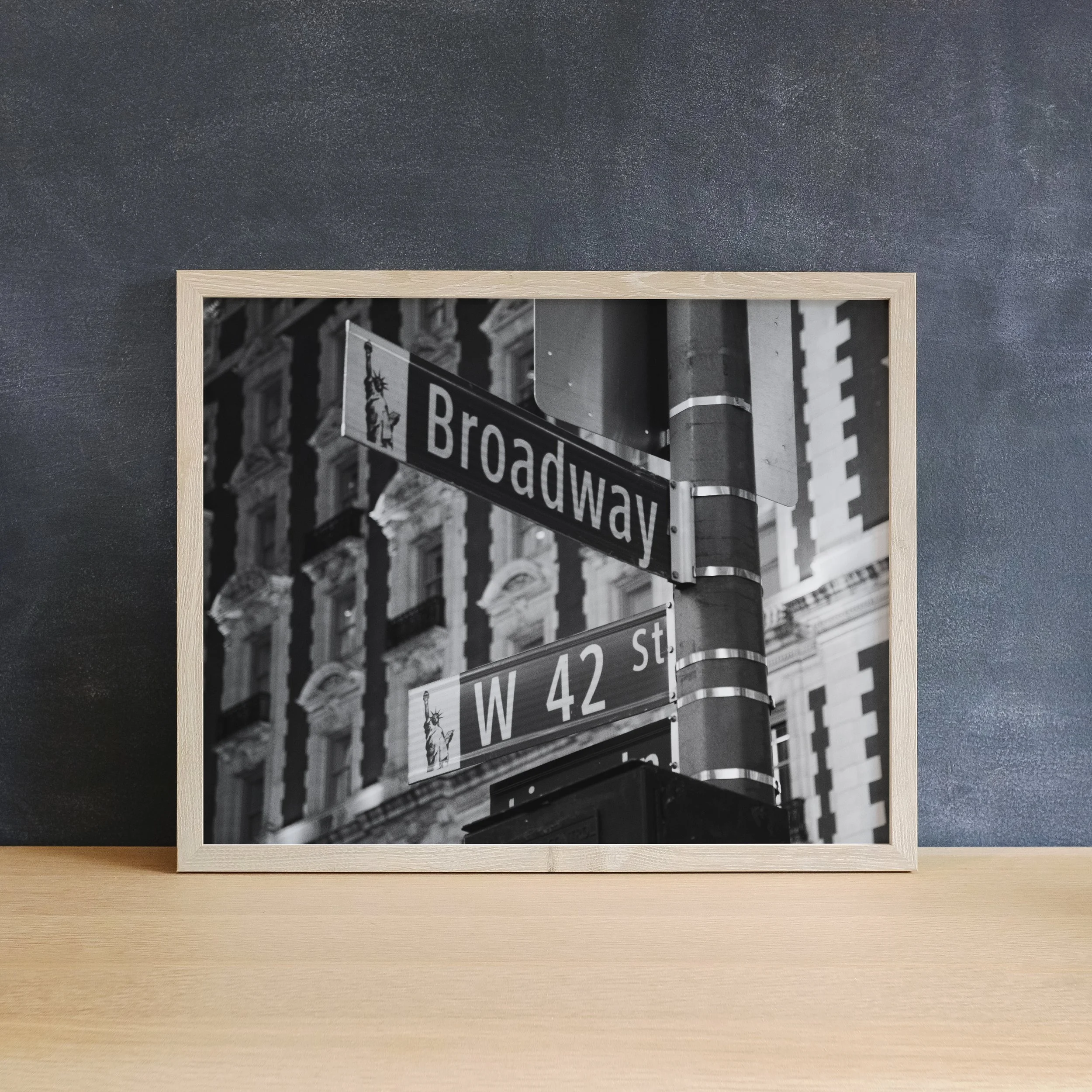 Light wood framed Broadway Noir poster leaning against a dark charcoal wall, a classic piece of New York wall art.