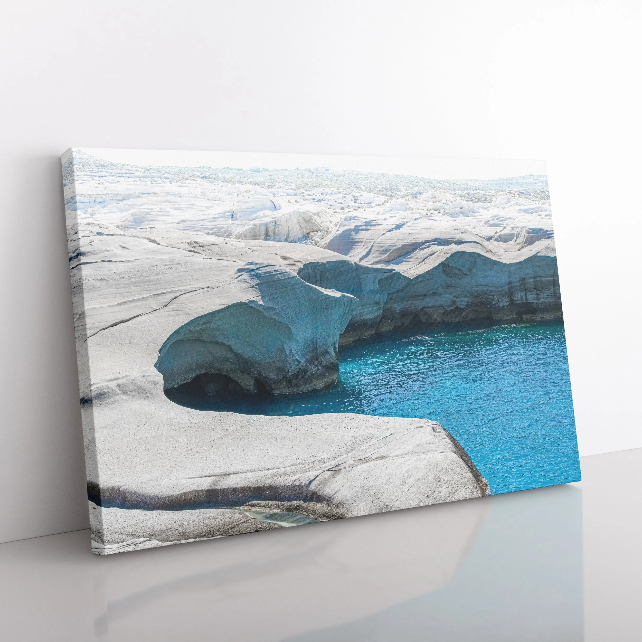 Angled side view of a Sarakiniko Beach gallery-wrapped canvas showing the distinct white lunar landscape and brilliant blue Aegean Sea, resting against a white wall.
