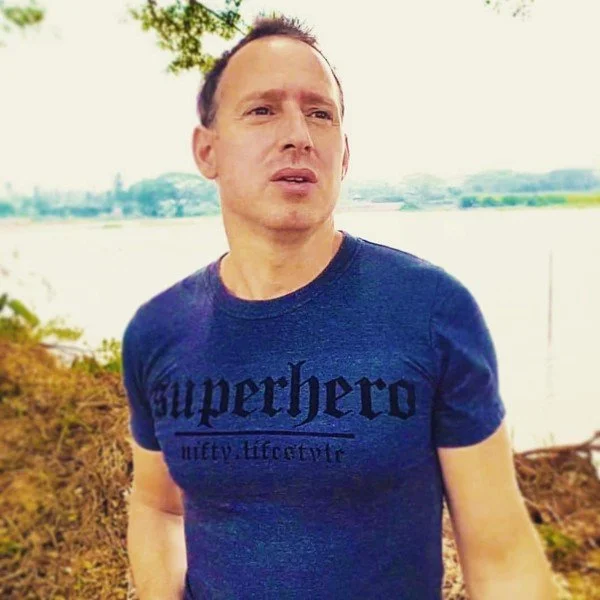 Chris Zanetti wearing Superhero T-shirt standing outdoors beside a lake.