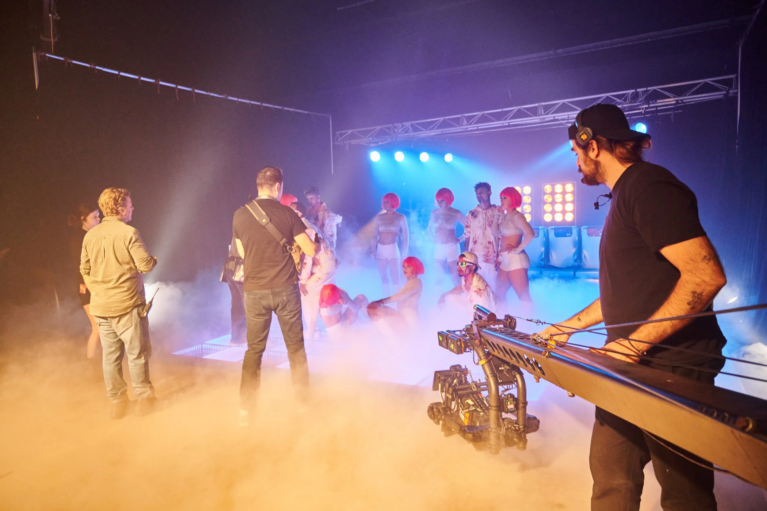 Filmmakers filming a scene with performers in costumes on stage, with fog and blue stage lights.