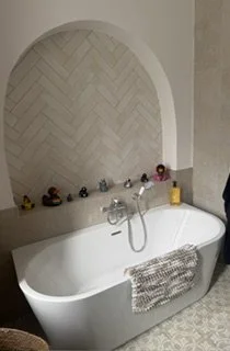 Baignoire blanche dans une salle de bain avec un miroir en arc et des objets de bain sur le rebord.