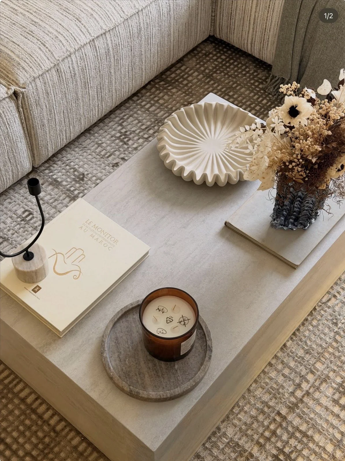 Table avec livres, vase de fleurs, plateau, bougie, et décoration dans un salon élégant.