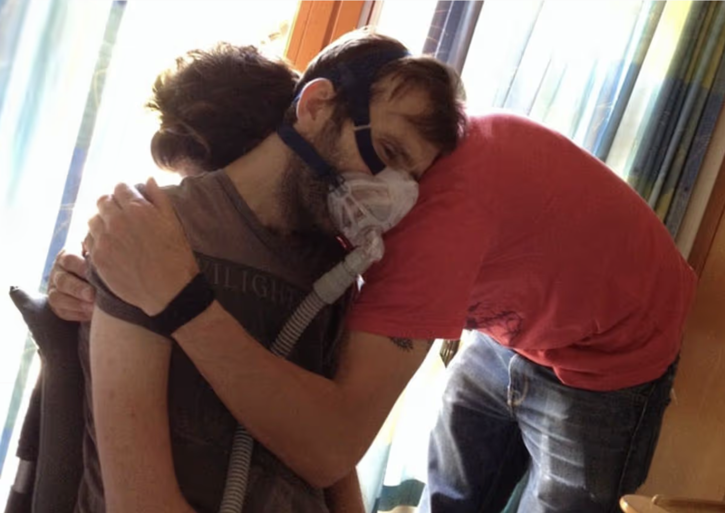 Two people hugging each other in a room with large windows and curtains.