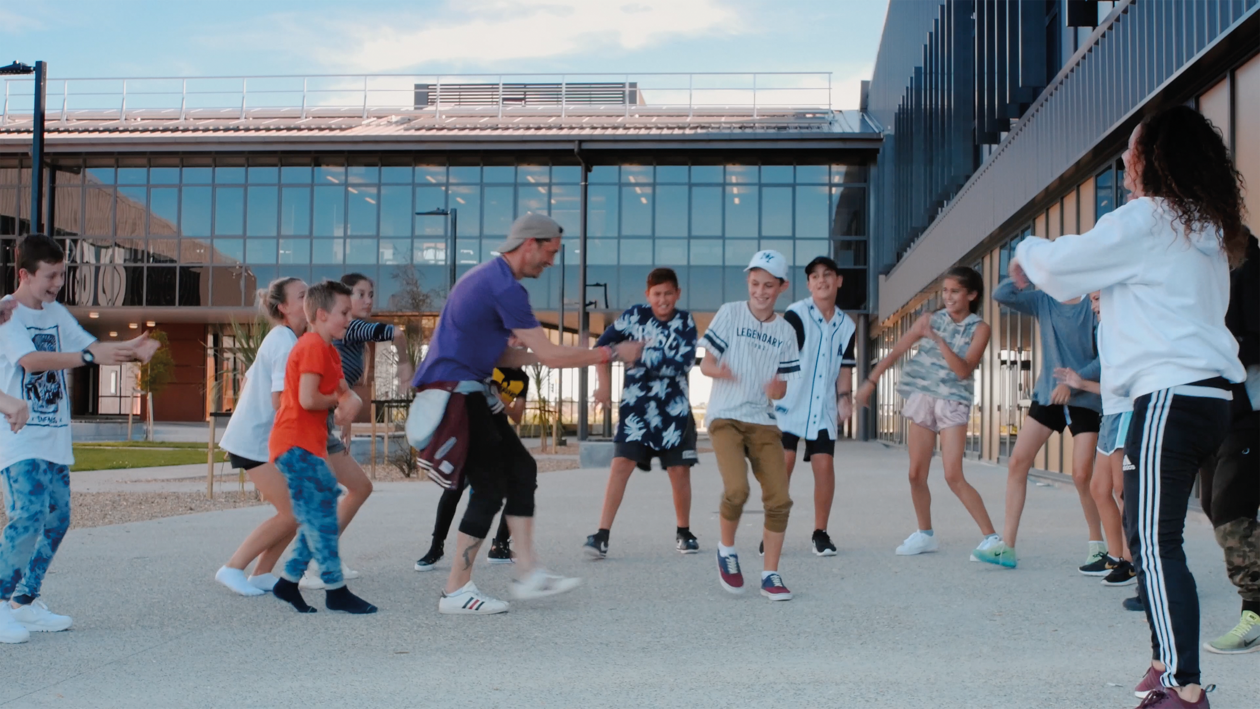 Children and a man playing a game outside in front of a modern glass building, enjoying an outdoor activity.