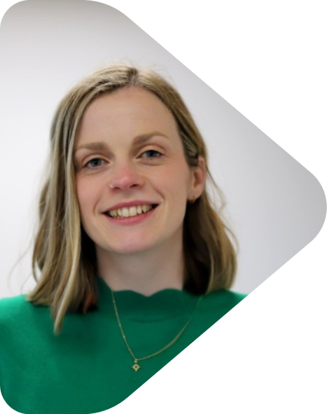 Founder of Flint & Arrow, Kit Powney, with shoulder-length blonde hair, wearing a green top and a gold necklace with a star pendant, standing against a plain light background.