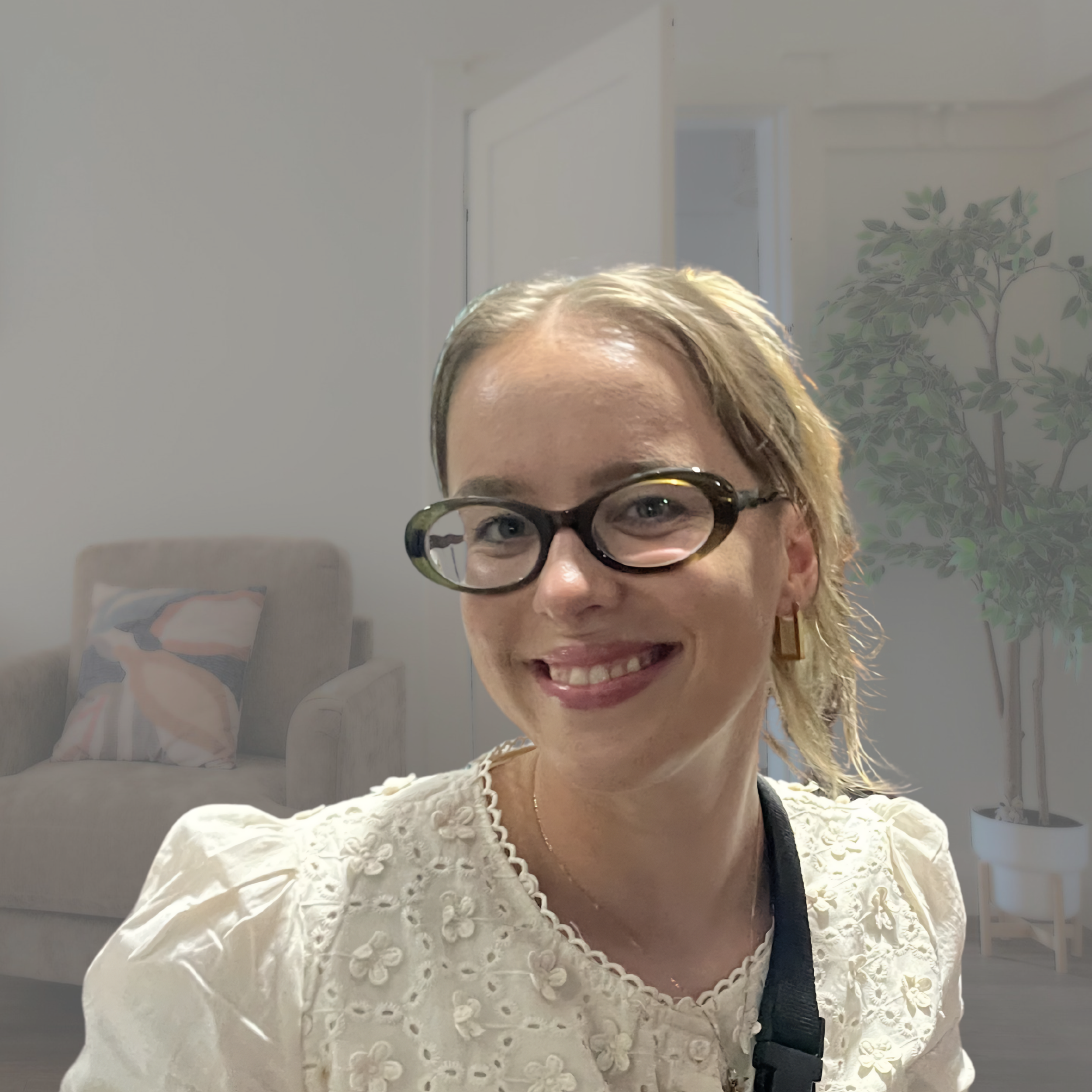 A woman with blonde hair, glasses, and a lace blouse smiling, with a background featuring a decorative tree illustration.