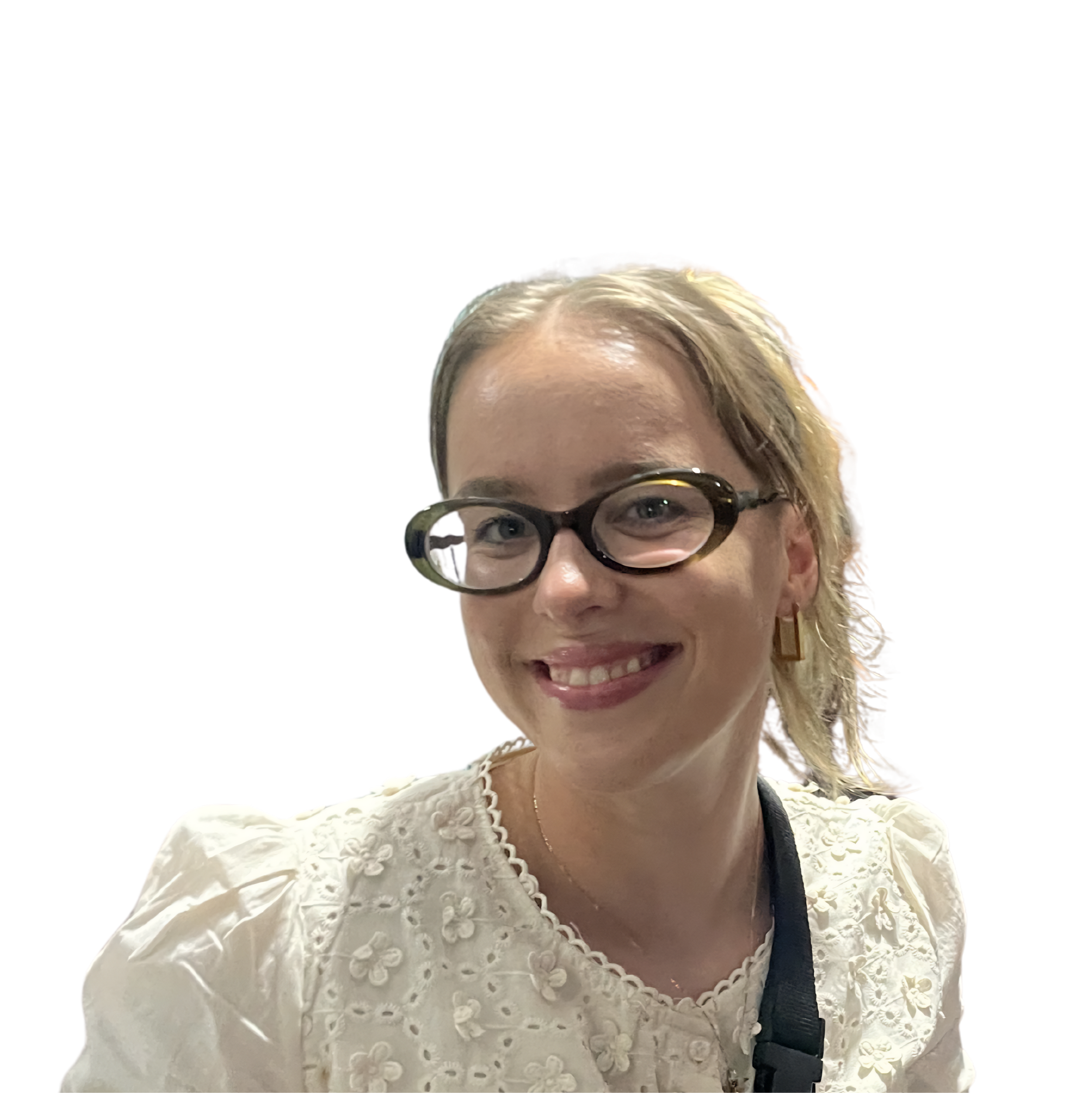 A woman with blonde hair, glasses, and a pearly smile, wearing a white dress with floral embroidery, smiling at the camera.