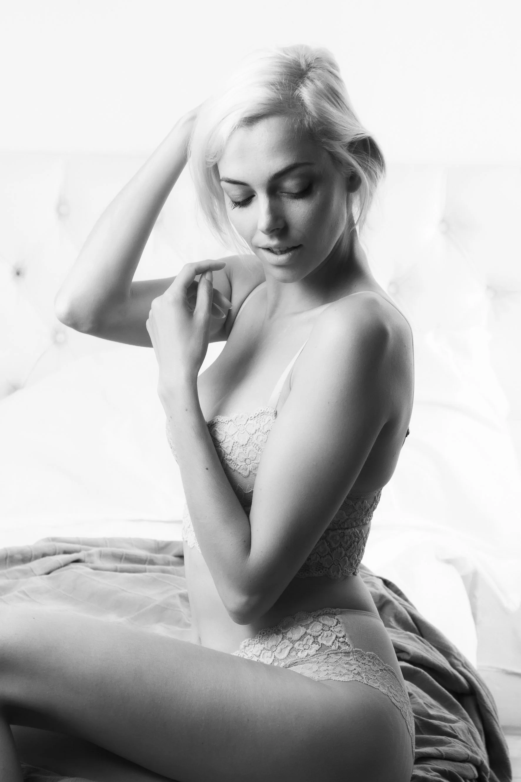 Black-and-white boudoir portrait of a woman in white lace lingerie on a bed, Antwerp studio
