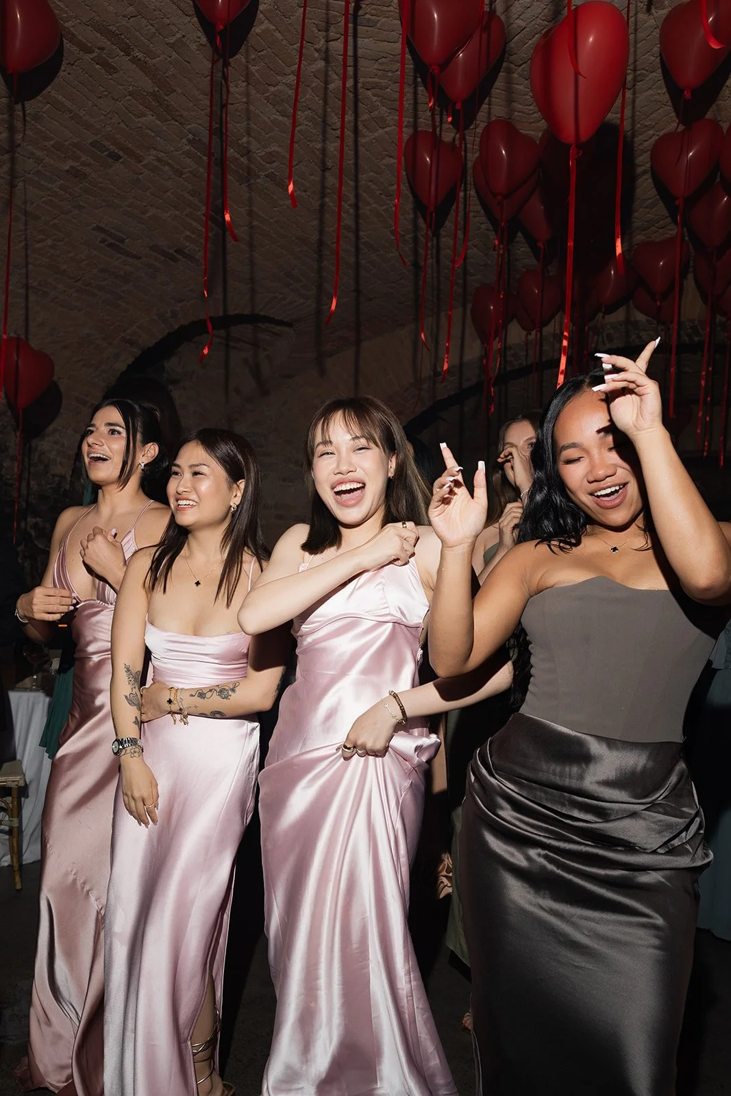 Gruppe von Frauen, die bei einer Party tanzen und lachen, Dekoration aus roten Herzballons im Hintergrund.