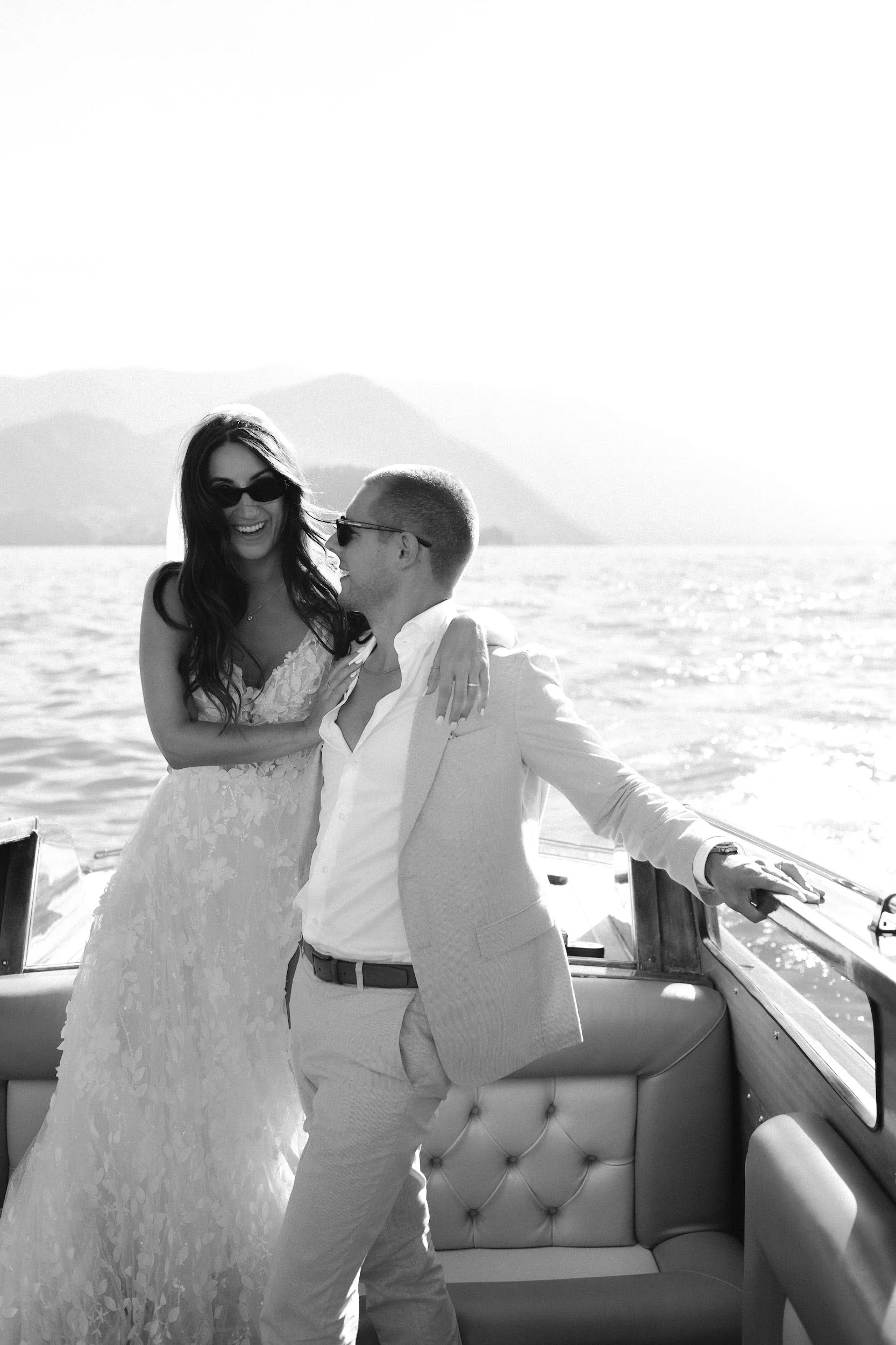 Ein glückliches Paar bei einer Hochzeit auf einem Boot auf dem Wasser mit Bergen im Hintergrund, in Schwarz-Weiß