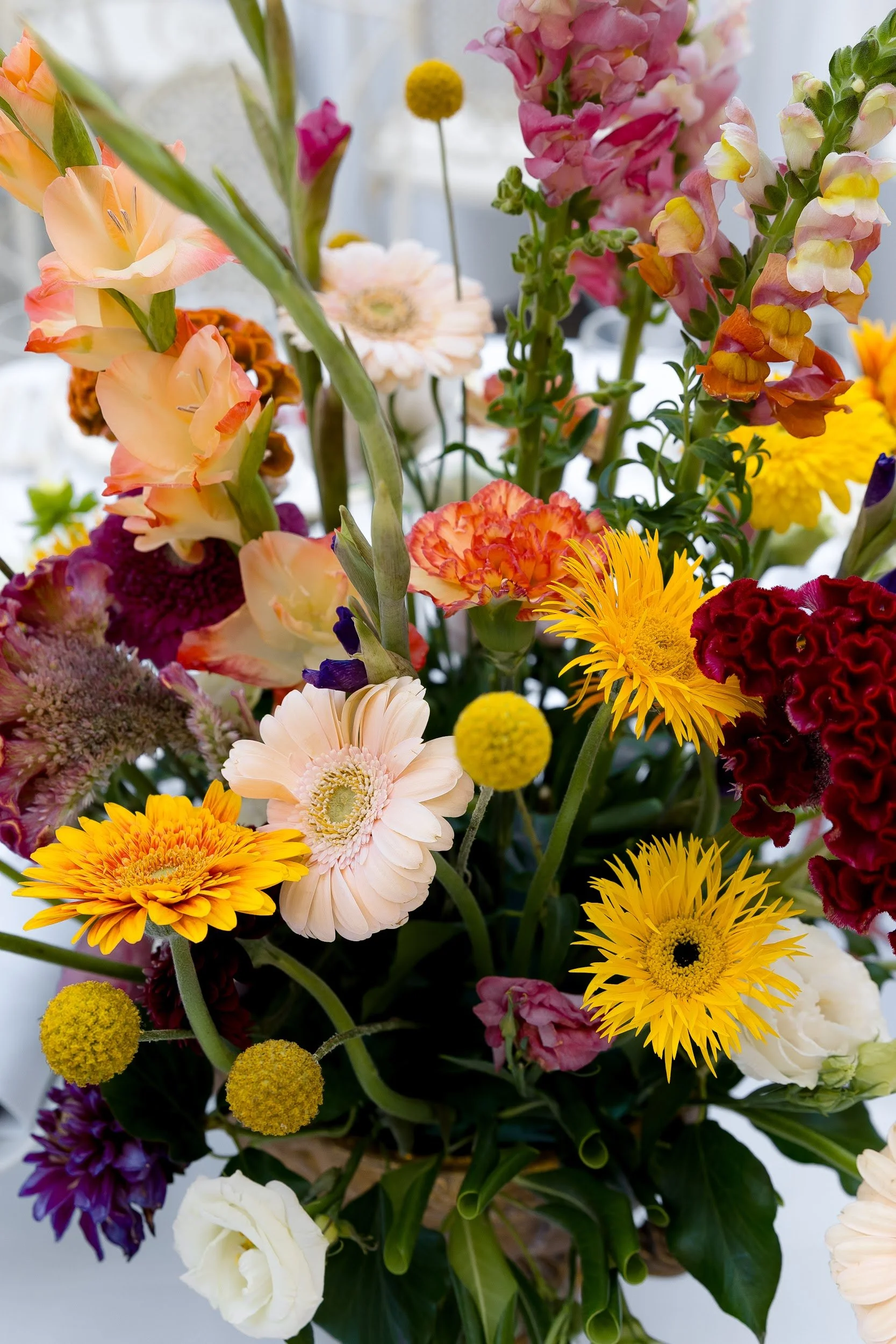Ein bunter Blumenstrauß mit verschiedenen Blumenarten in verschiedenen Farben, darunter gelbe, orange, rosa, lila und weiße Blumen, vor einem hellen Hintergrund.