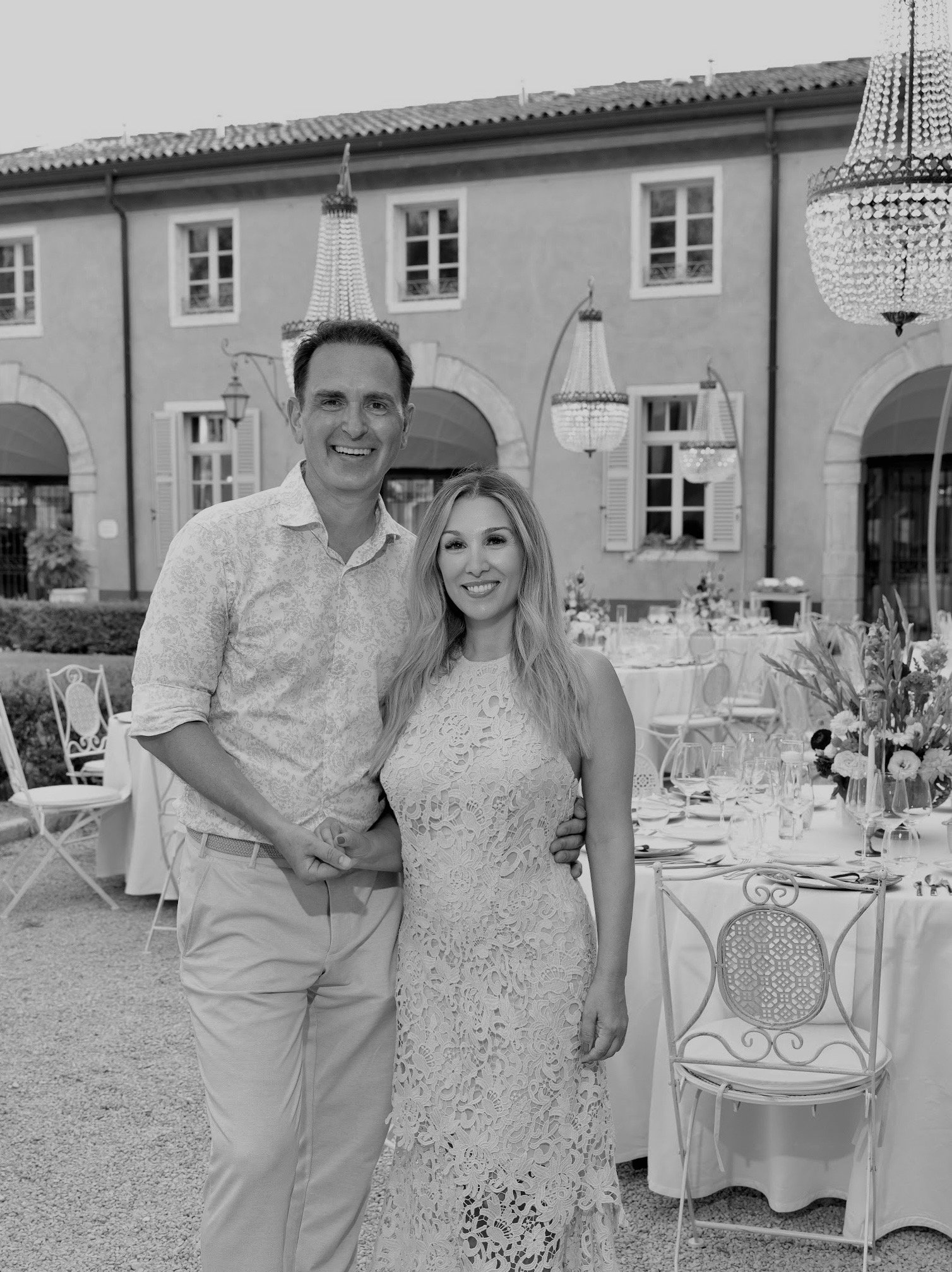 Ein lachendes Paar beim Dinner im Freien, mit schön gedecktem Tisch und einem historischen Gebäude im Hintergrund.