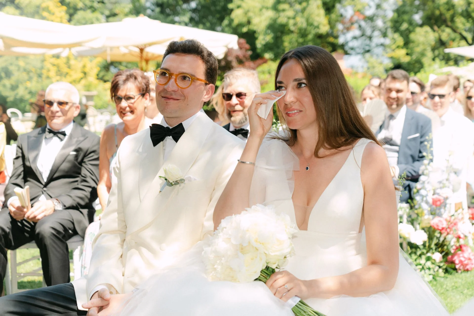 Braut und Bräutigam bei einer Hochzeit im Freien, die Braut weint beim Auszug, während die Gäste im Hintergrund lachen und den Moment genießen.