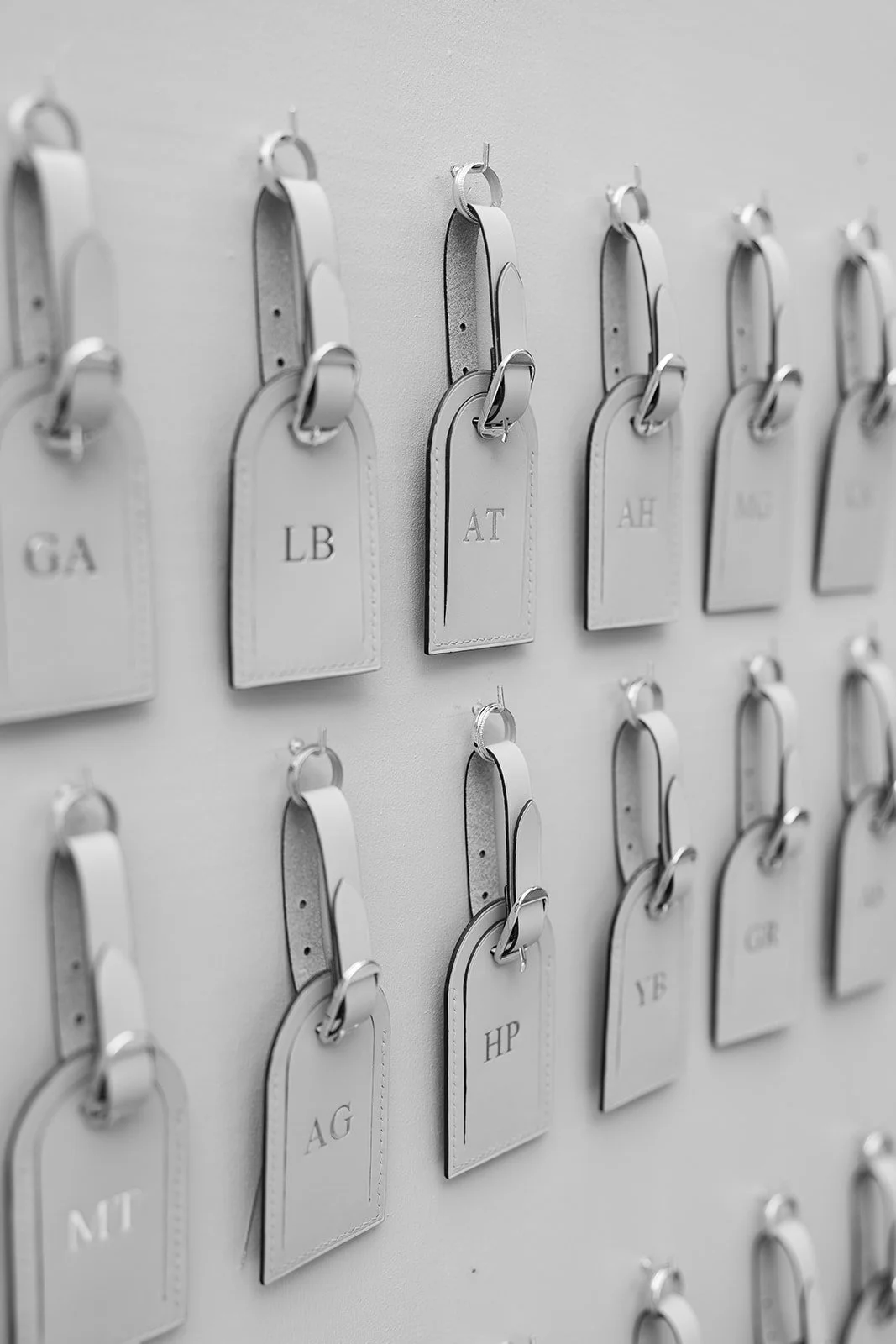 Weiße Leder-Schirmen mit eingravierten Initialen, aufgehängt an Haken an einer weißen Wand.