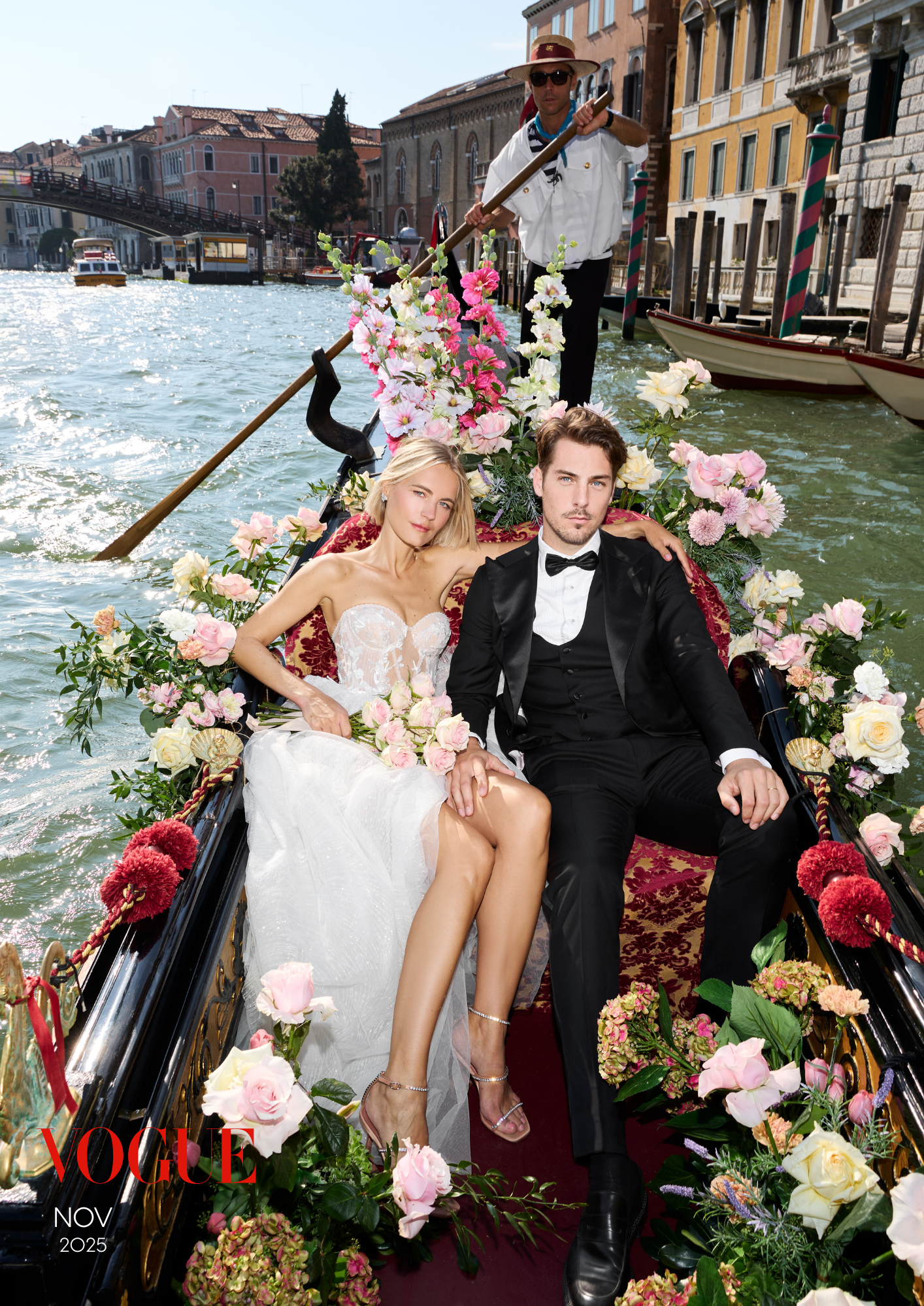 Ein düsterer Mann in Smoking sitzend auf einem Blumenboot in Venedig, umgeben von vielen bunten Blumen, mit einer Frau in einem weißen Brautkleid an seiner Seite. Im Hintergrund sind Gebäude, Boote und eine Gondel zu sehen.