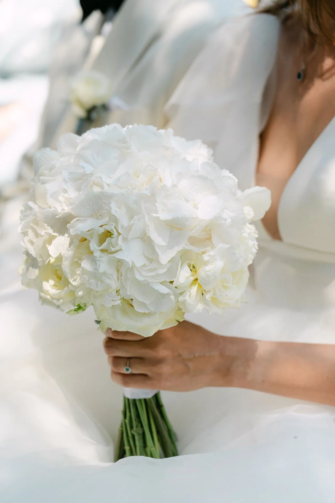 Eine Hochzeitsbraut hält einen weißen Blumenstrauß aus Hydrangea und Orchideen, umgeben von ihrem Hochzeitskleid.