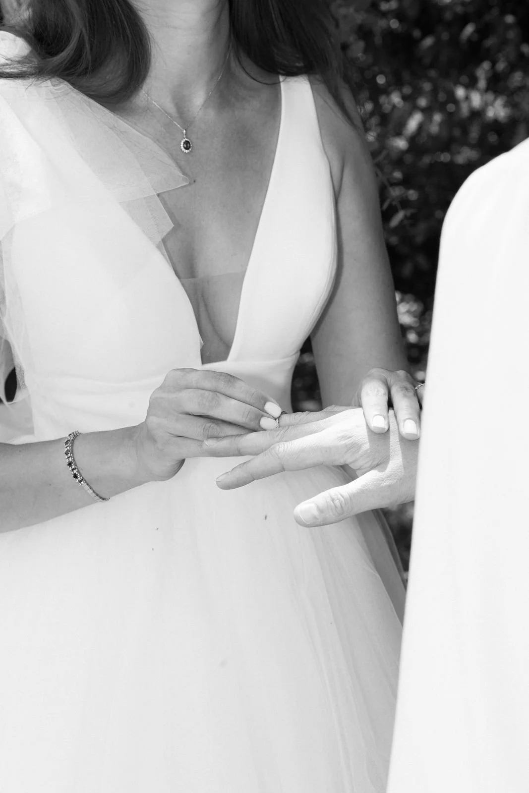 Schwarz-weiß-Bild einer Frau in einem weißen Brautkleid, die die Hand eines Mannes hält und bei einer Zeremonie oder Hochzeit beteiligt ist.