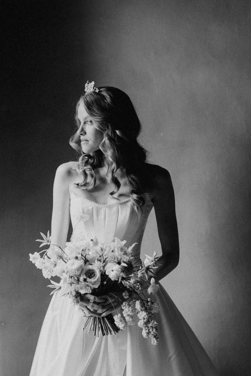 Schwarz-weiß-Fotografie einer Frau in Brautkleid mit Blumenstrauß.