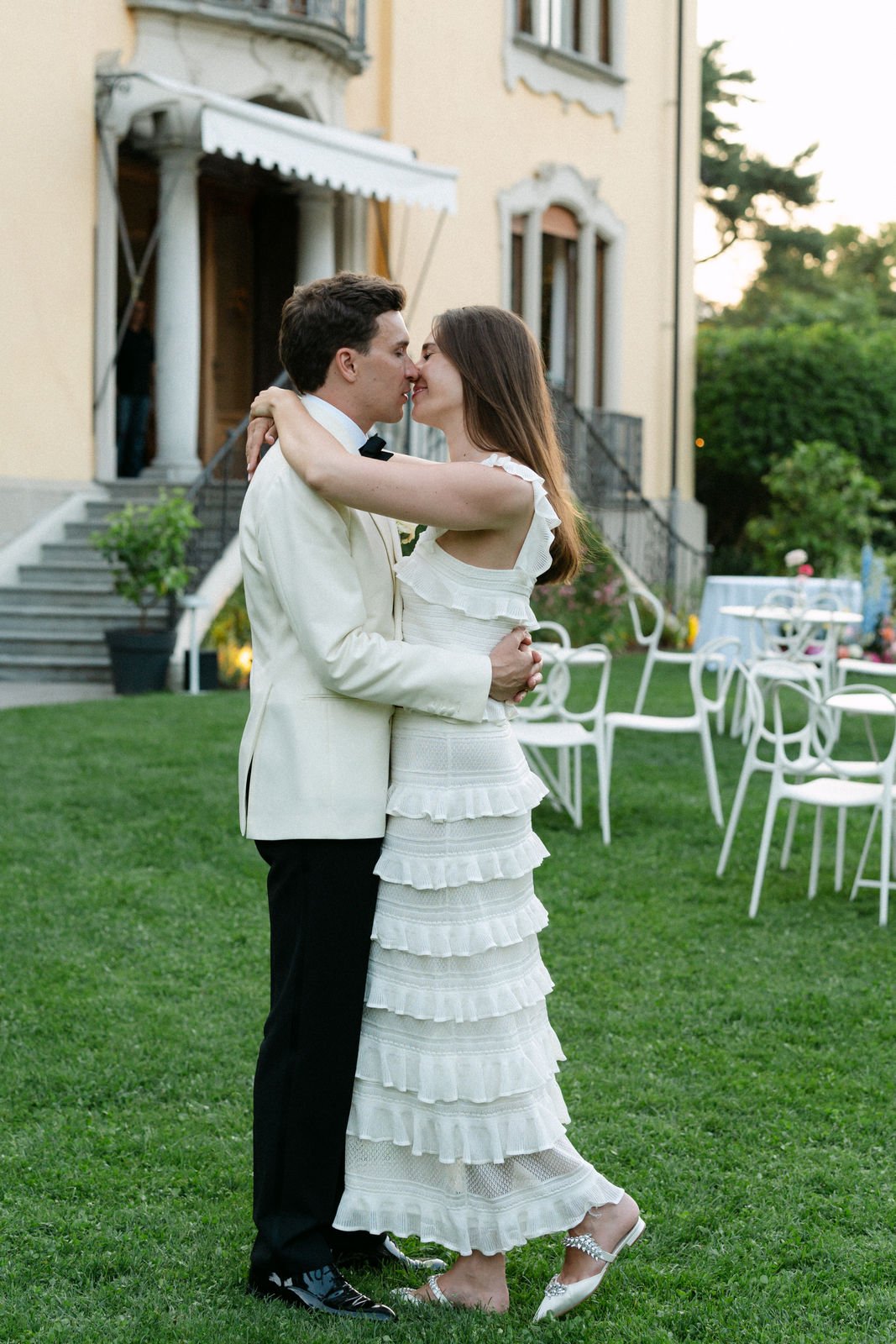 Ein Mann und eine Frau beim Tanz bei einer Hochzeit im Garten, im Hintergrund ein altes Gebäude und weiße Stühle.