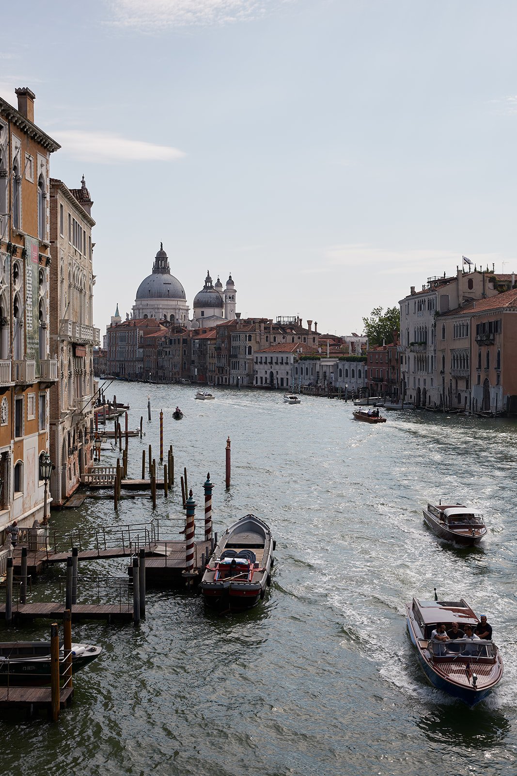 Ein Kanal in Venedig mit mehreren Booten, umgeben von historischen Gebäuden und einer Kuppel im Hintergrund.