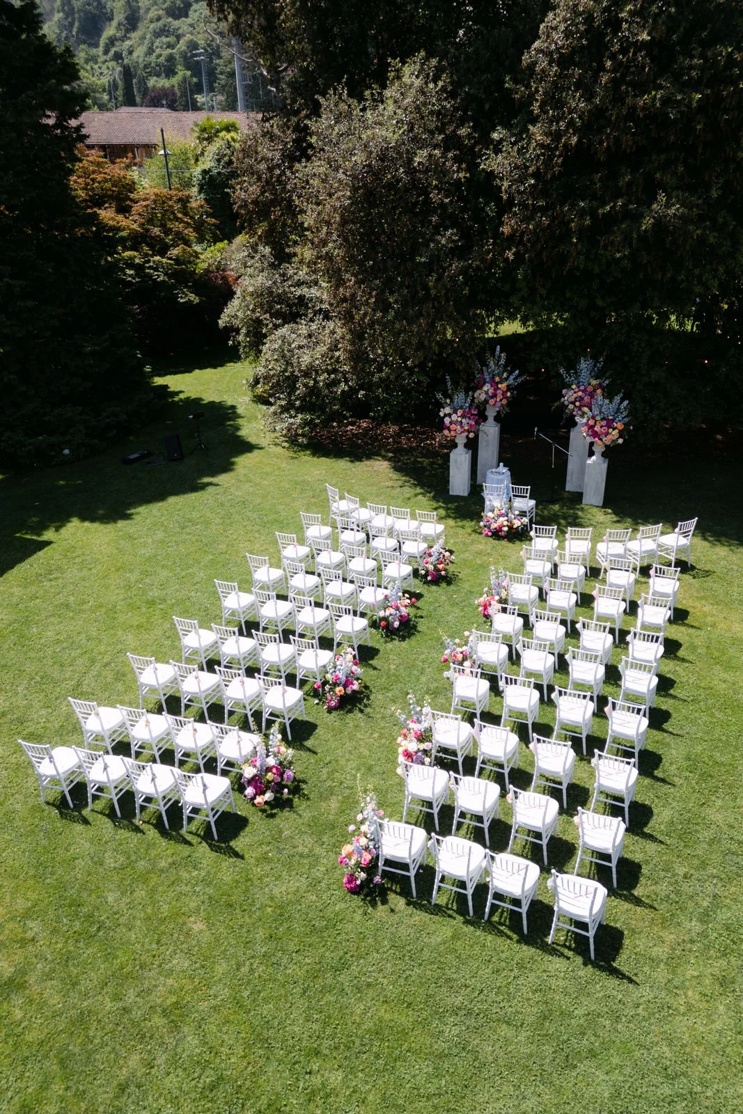 Ein Garten mit zeremoniellem Bereich, bestehend aus weißen Stühlen, Blumenarrangements und einem Altar mit Blumen, vorbereitet für eine Hochzeit im Freien.
