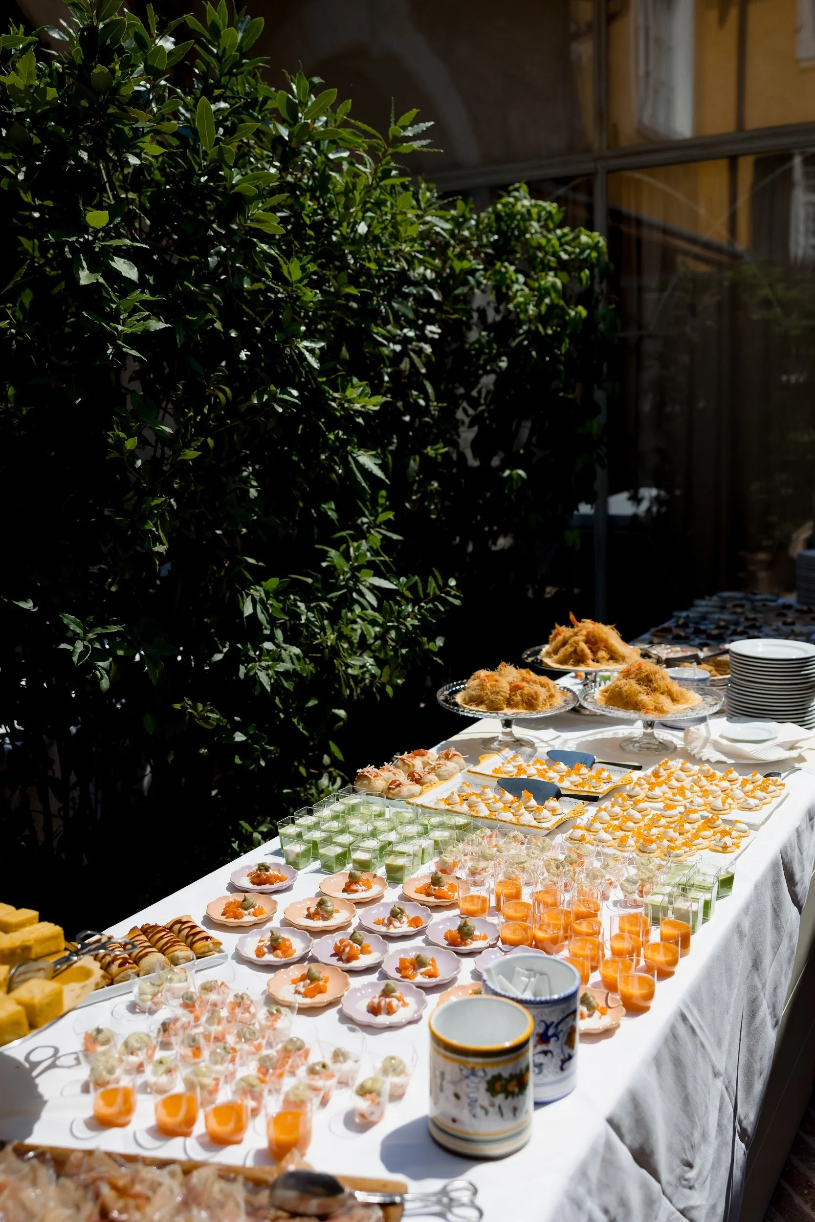 Ein Buffettisch mit verschiedenen kleinen Speisen und Desserts, bei Tageslicht im Freien, umgeben von Grün und einer Kälteaufnahme