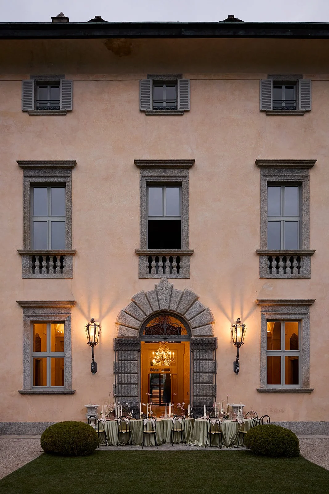 Historisches Gebäude mit mehreren Fenstern, laternenbeleuchteter Eingang und einem festlich gedeckten Tisch im Garten.