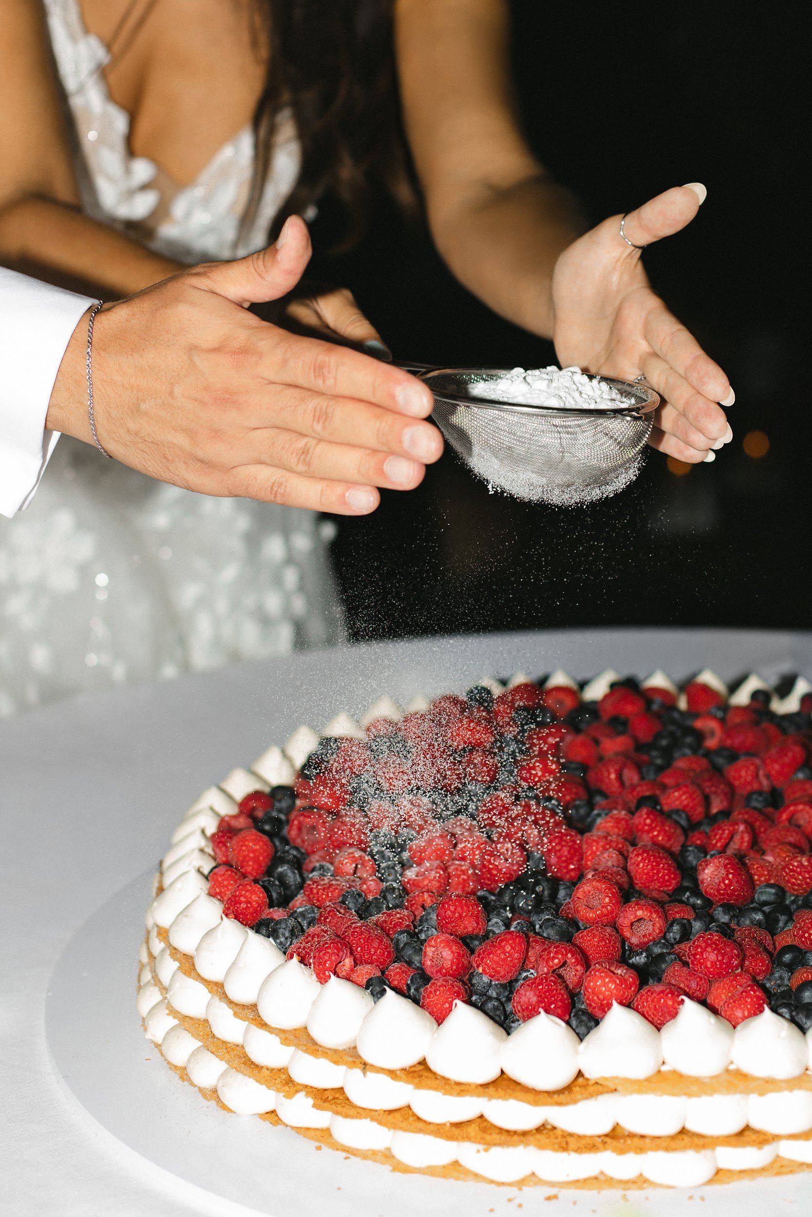 Nahaufnahme eines zweistöckigen Obstkuchens mit Biskuitboden, einer Schicht Schlagsahne, frischen Beeren und einer Dekoration aus weißen Baisers, die rings um den Kuchen gelegt sind.