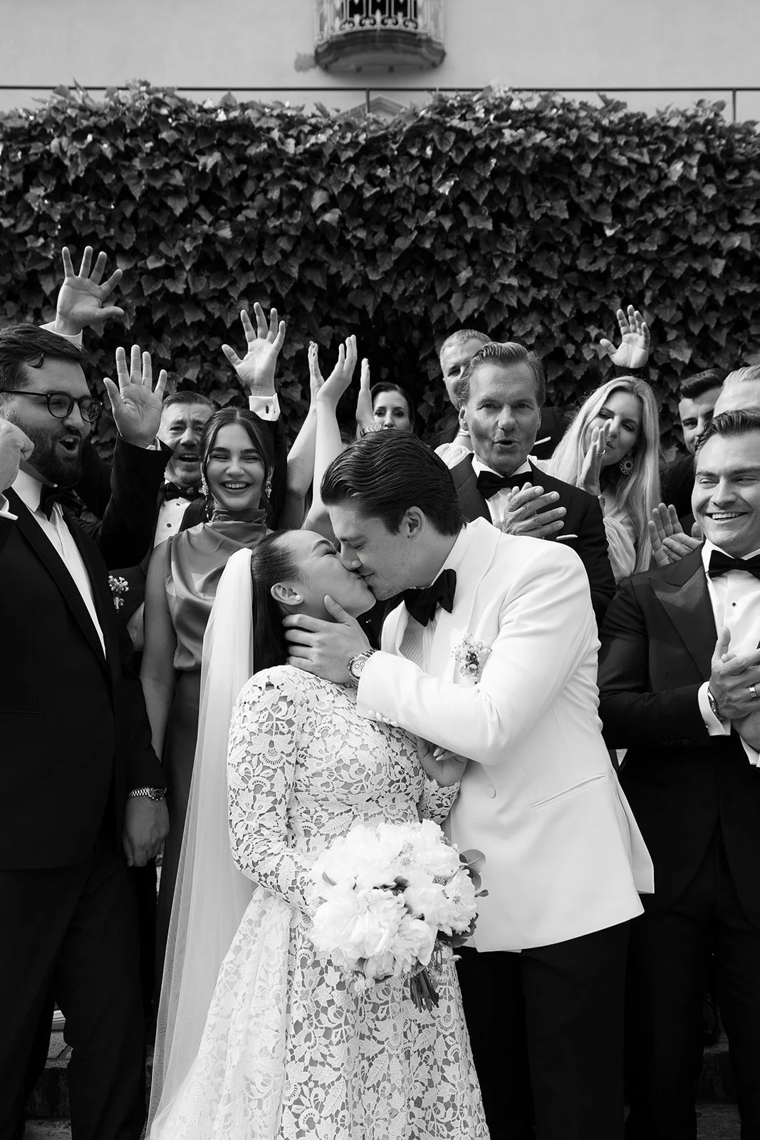 Hochzeitspaar küsst sich, umringt von feiernden Gästen bei einer schwarzen und weißen Hochzeitsfeier.
