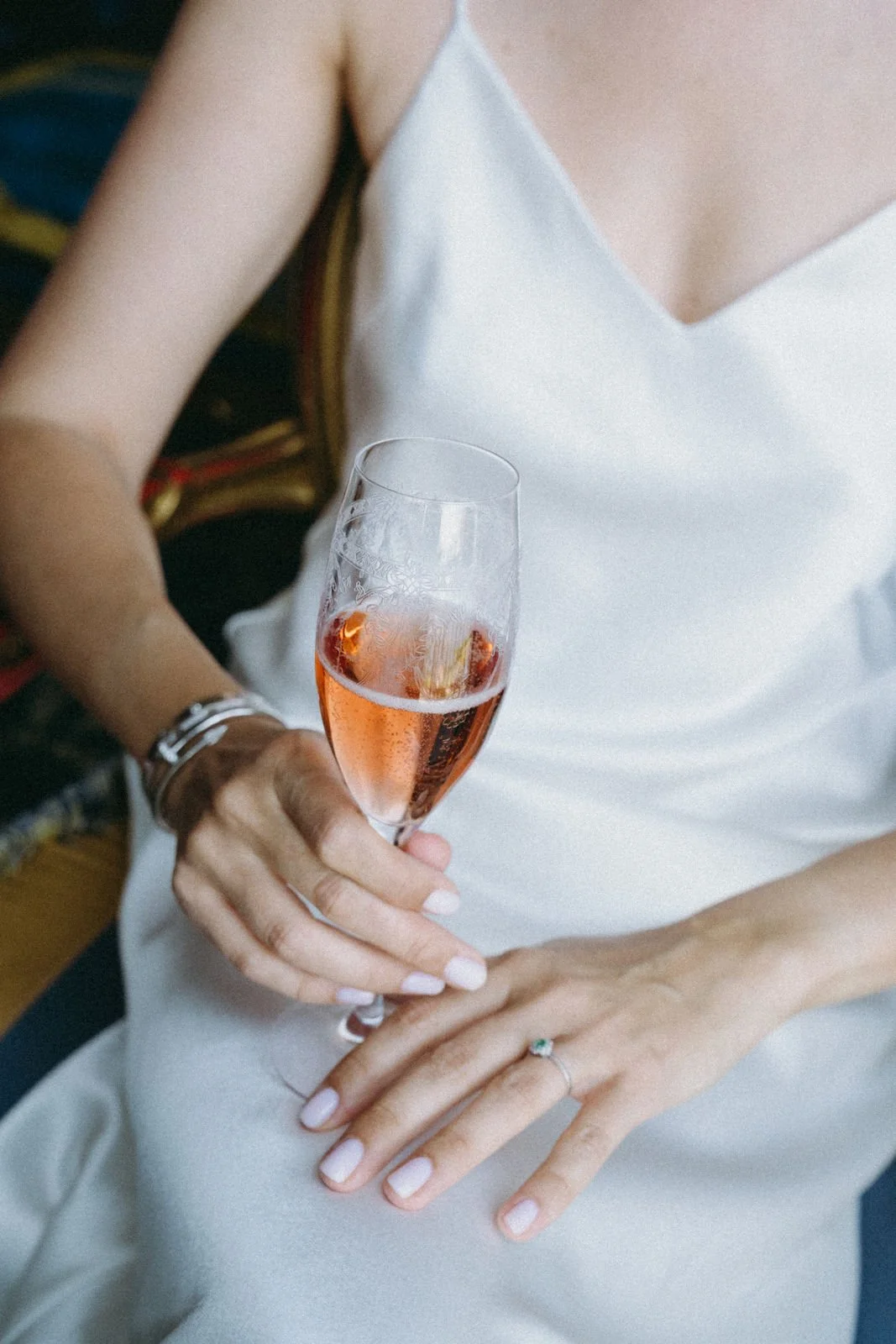Frau in weißem Kleid hält ein Glas Rosé-Sekt mit Eiswürfeln in der Hand.