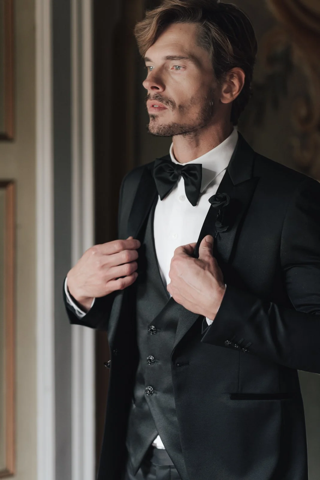 Mann in eleganter schwarzer Anzug mit Fliege, der die Jacke seines Sakkos verschließt.