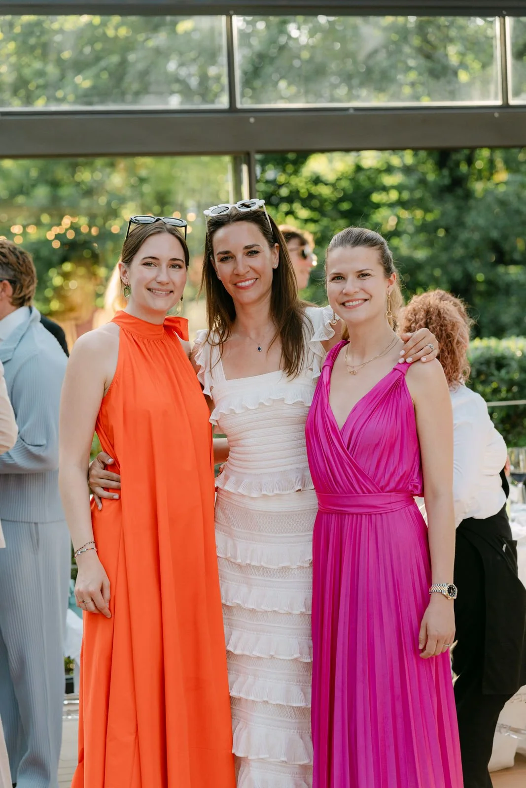 Drei junge Frauen in eleganten Kleidern beim Feiern im Freien, lächelnd und zusammenstehend