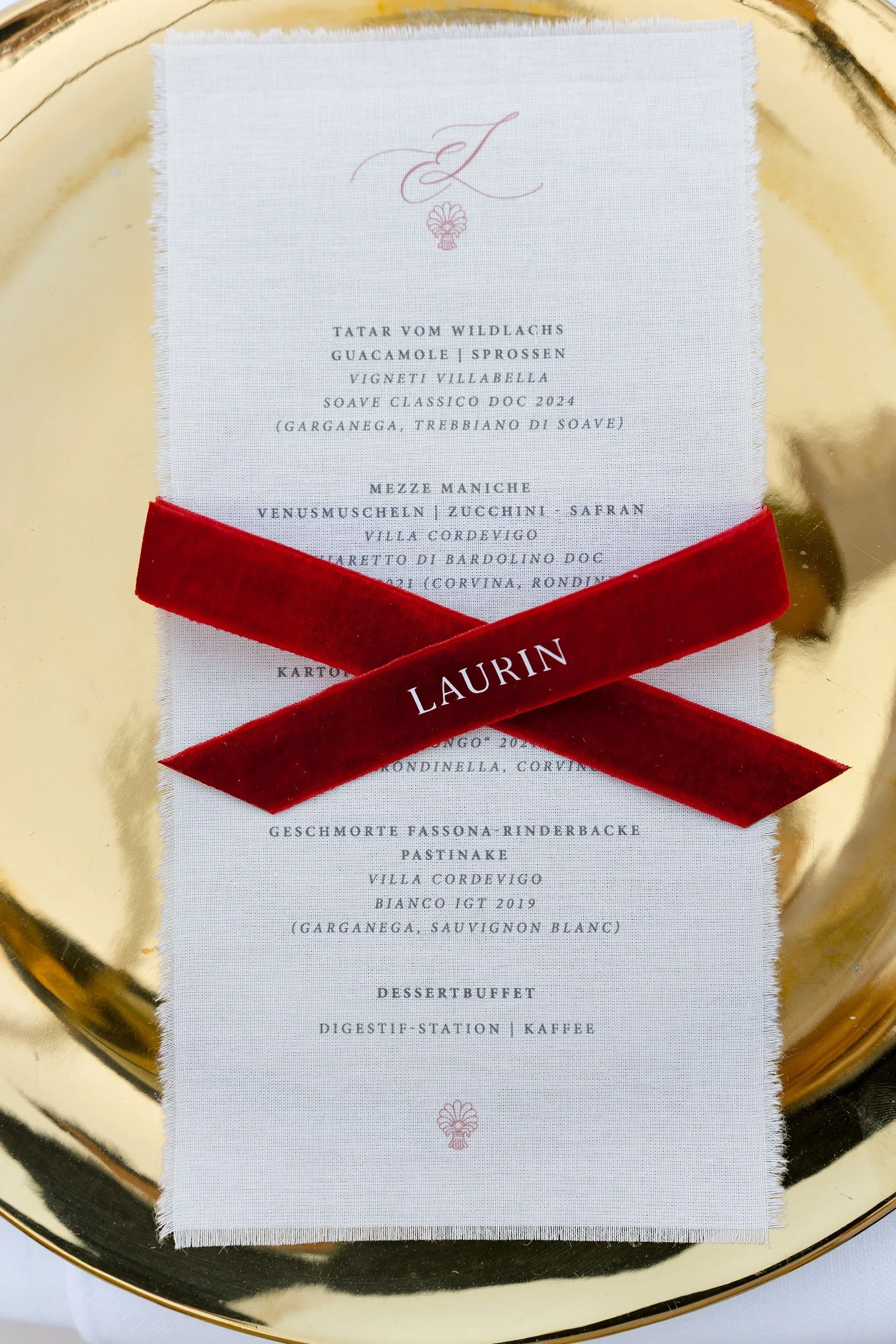 Speisekarte auf einem weißen Tuch mit rotem Band, das den Namen Laurin trägt, auf einer goldfarbenen runden Oberfläche