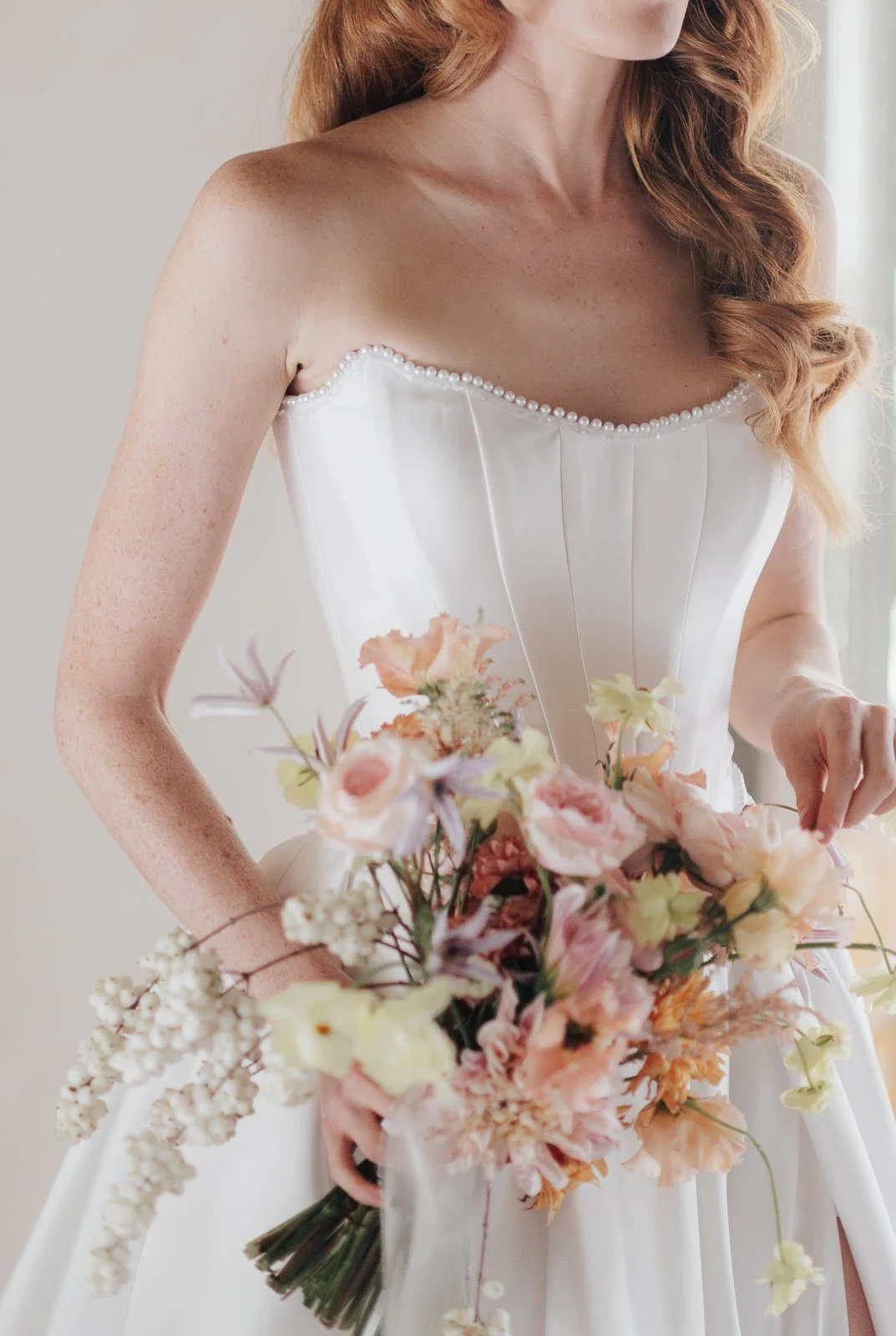 Eine Frau in einem weißen Brautkleid hält einen Blumenstrauß mit pastellfarbenen Blumen.