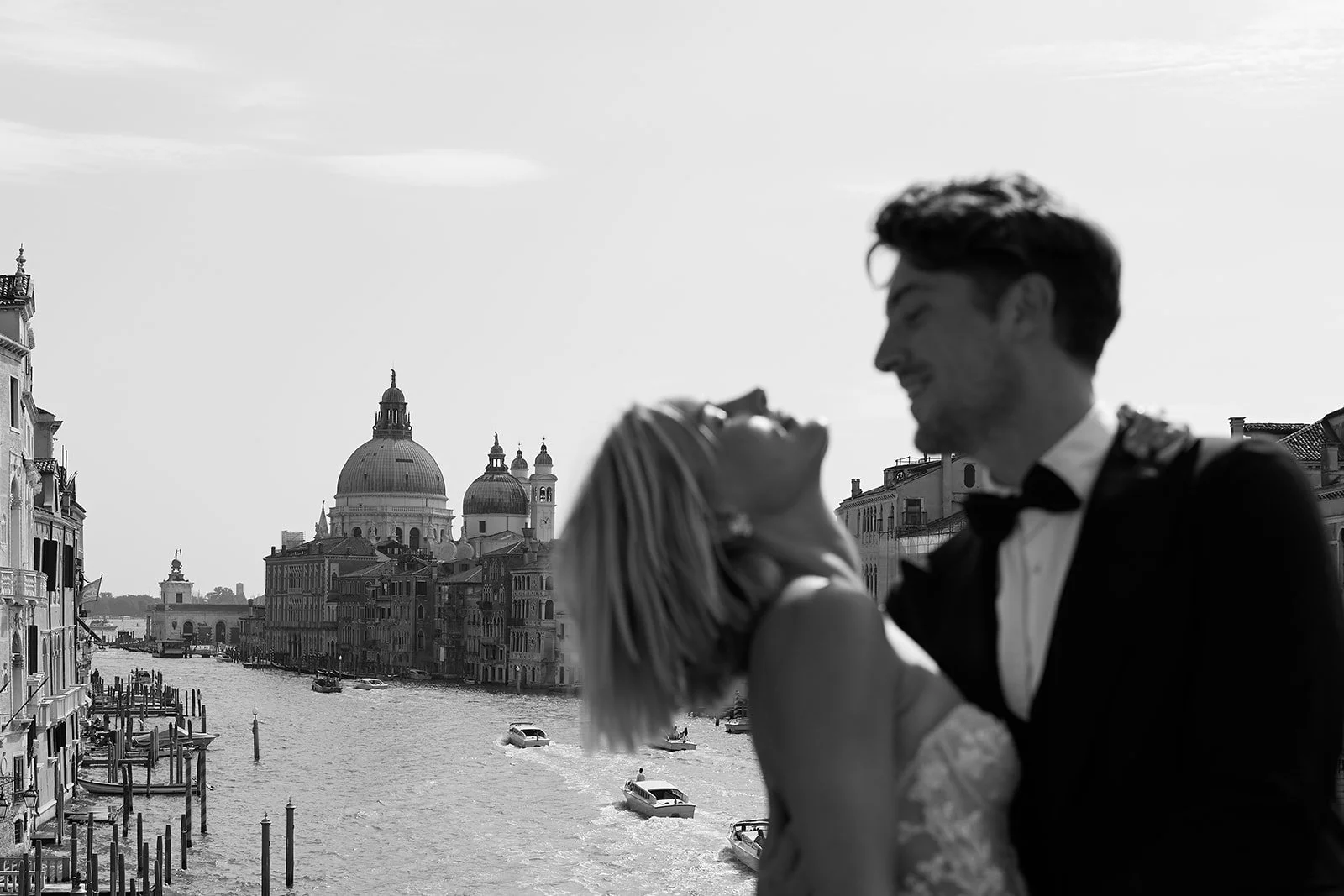 Ein lachendes Paar in formeller Kleidung am Kanal in Venedig, Italien, im Schwarz-Weiß-Foto.
