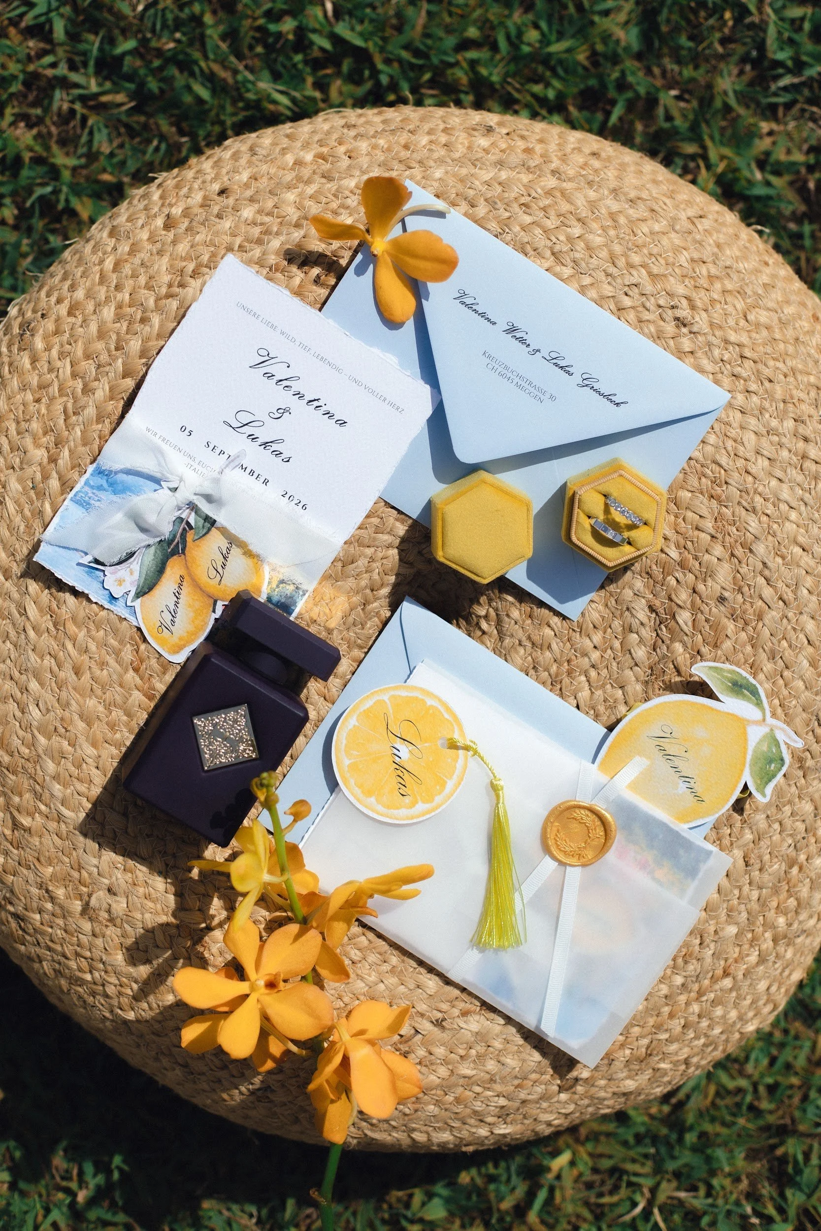 Hochzeitseinladungen, rosa und gelbe Blumen, ein Strauss, einer Ring in einer kleinen gelben Schmuckschatulle, eine gelbe Schutzkappe, eine Apple Schachtel auf einer geflochtenen Unterlage im Freien.