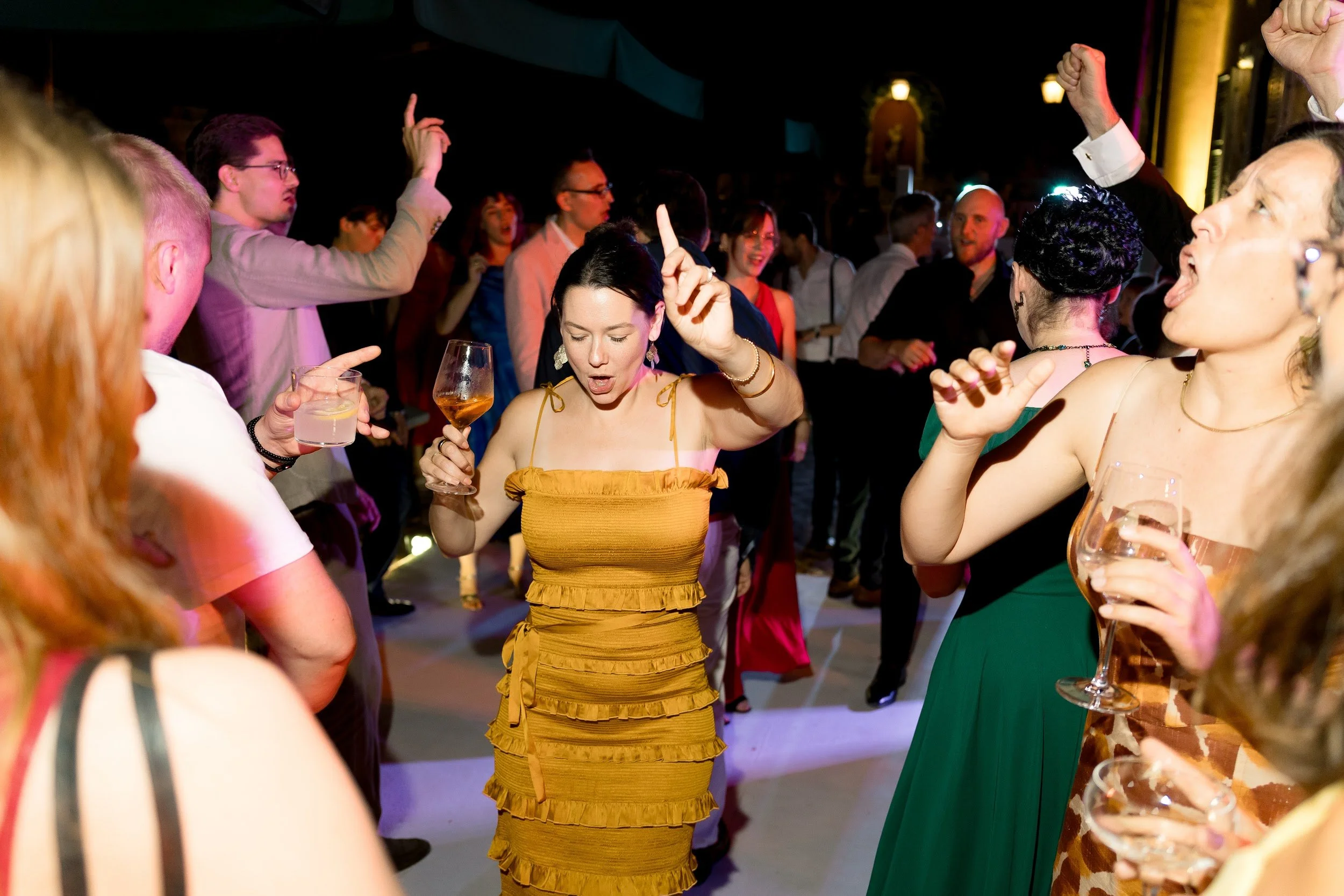 Menschen tanzen und feiern auf einer Party, einige halten Getränke in den Händen, im Hintergrund sind weitere Gäste zu sehen.