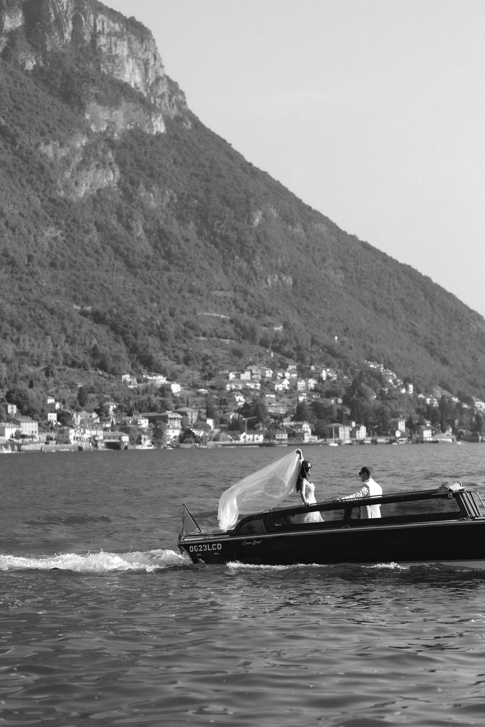 Ein Paar, das auf einem Boot auf einem See vor einer bergigen Landschaft steht.