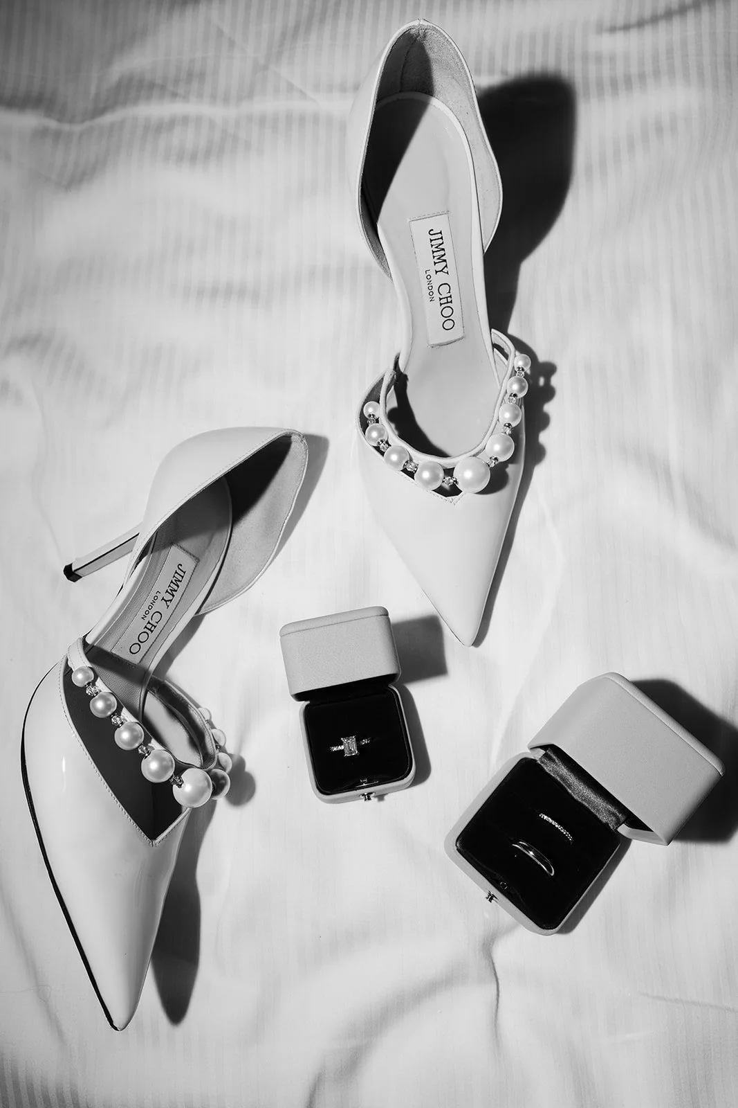 Ein Paar weiße High Heels mit Perlenverzierung, ein schlichter Ring in einer Schmuckbox, zwei weiße Boxen, wahrscheinlich Schmuckboxen.