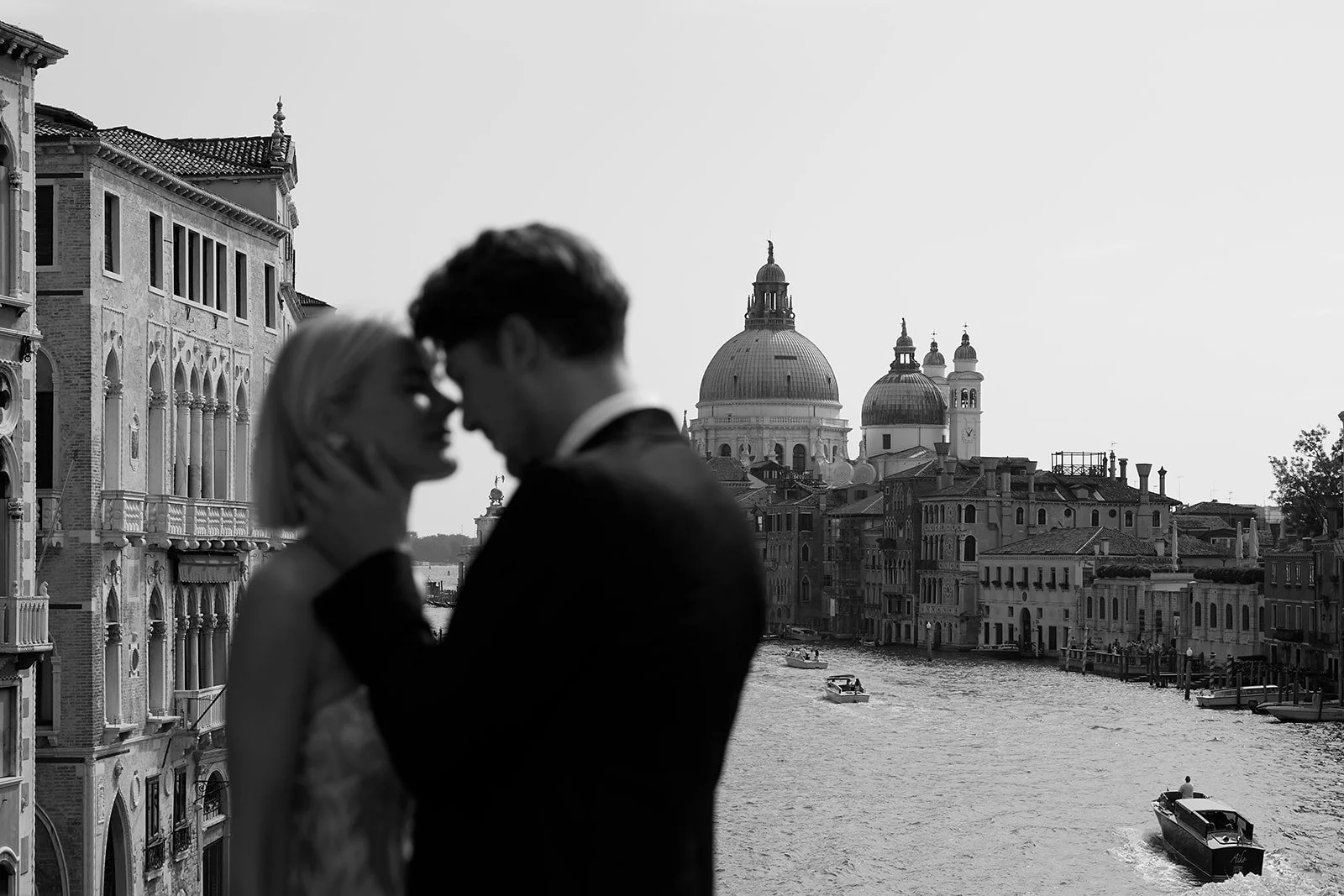 Ein Paar in Silhouette vor der Kulisse der Kanäle und historischen Gebäude Venedigs, mit Blick auf die Basilika Santa Maria della Salute im Hintergrund.